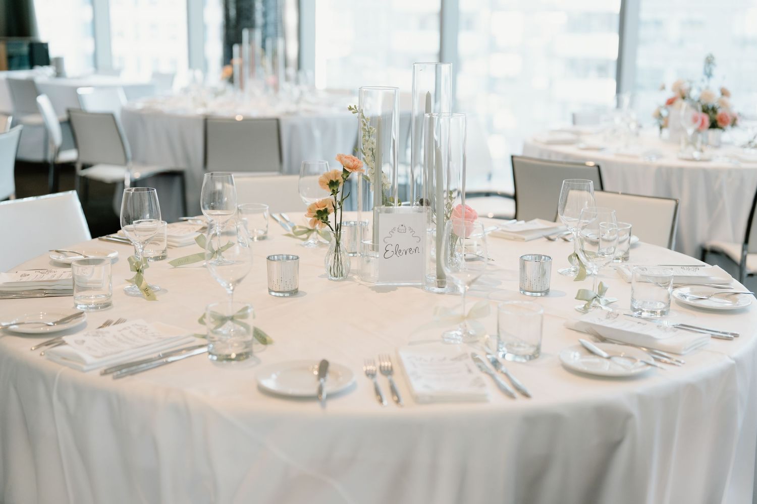 Elegant wedding reception table setting with white linens, delicate floral centerpieces and formal place settings.