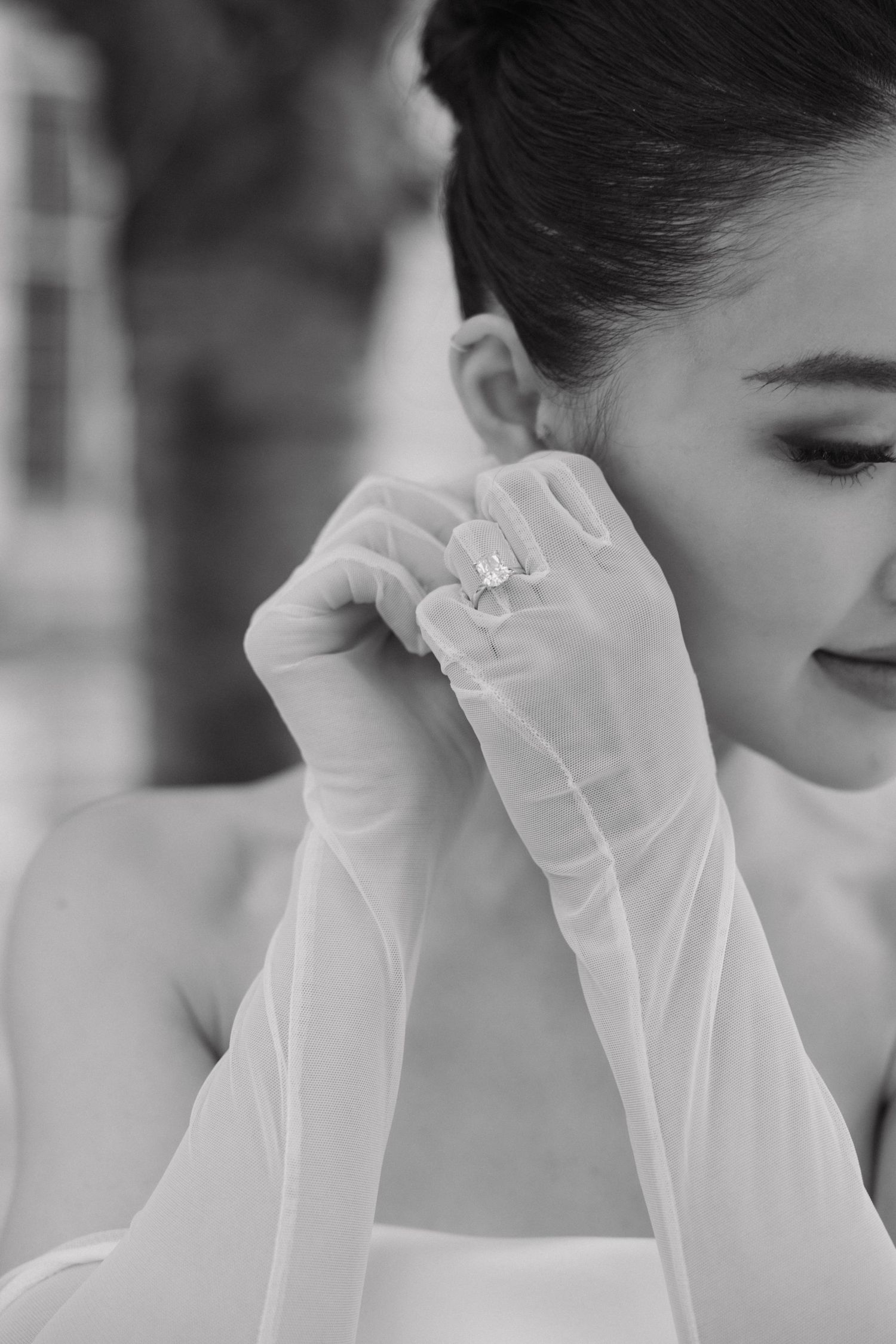 Black and white portrait of a bride in sheer long gloves and strapless gown delicately touching her face.