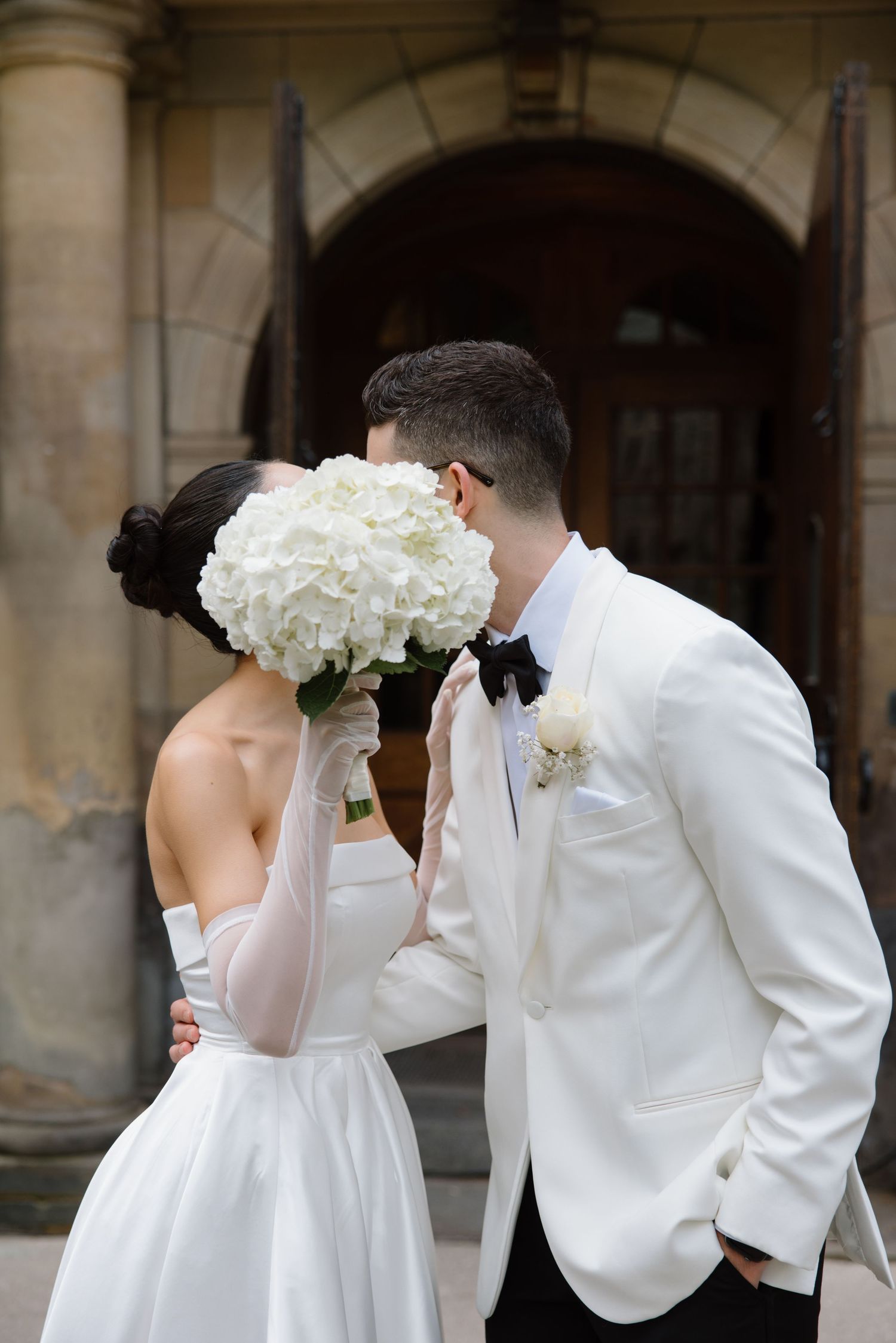 A bride and groom share a romantic moment behind a white hydrangea bouquet at their formal wedding.