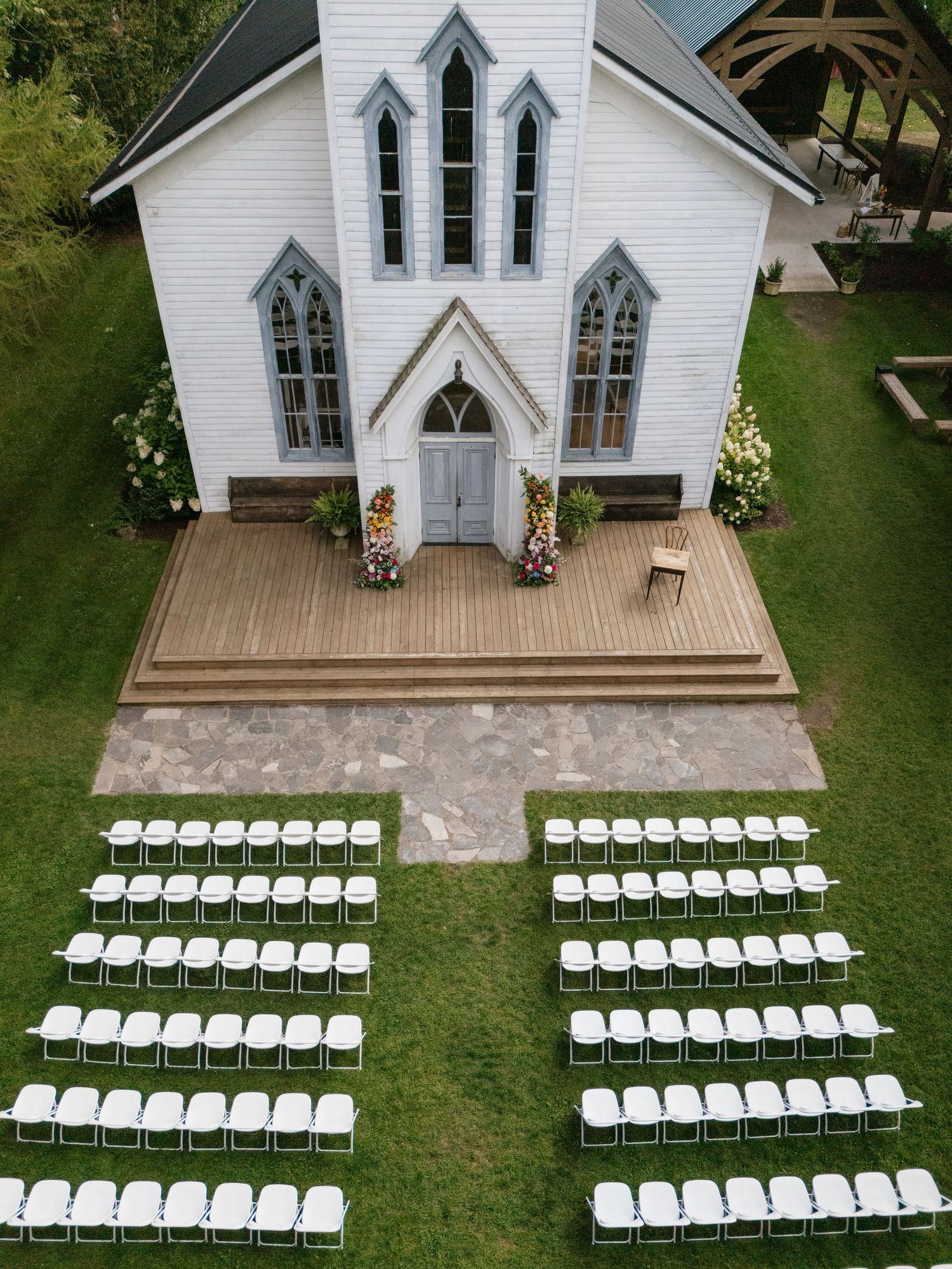Aerial view of a white chapel with rows of white chairs set up for an outdoor wedding ceremony on a wooden deck.