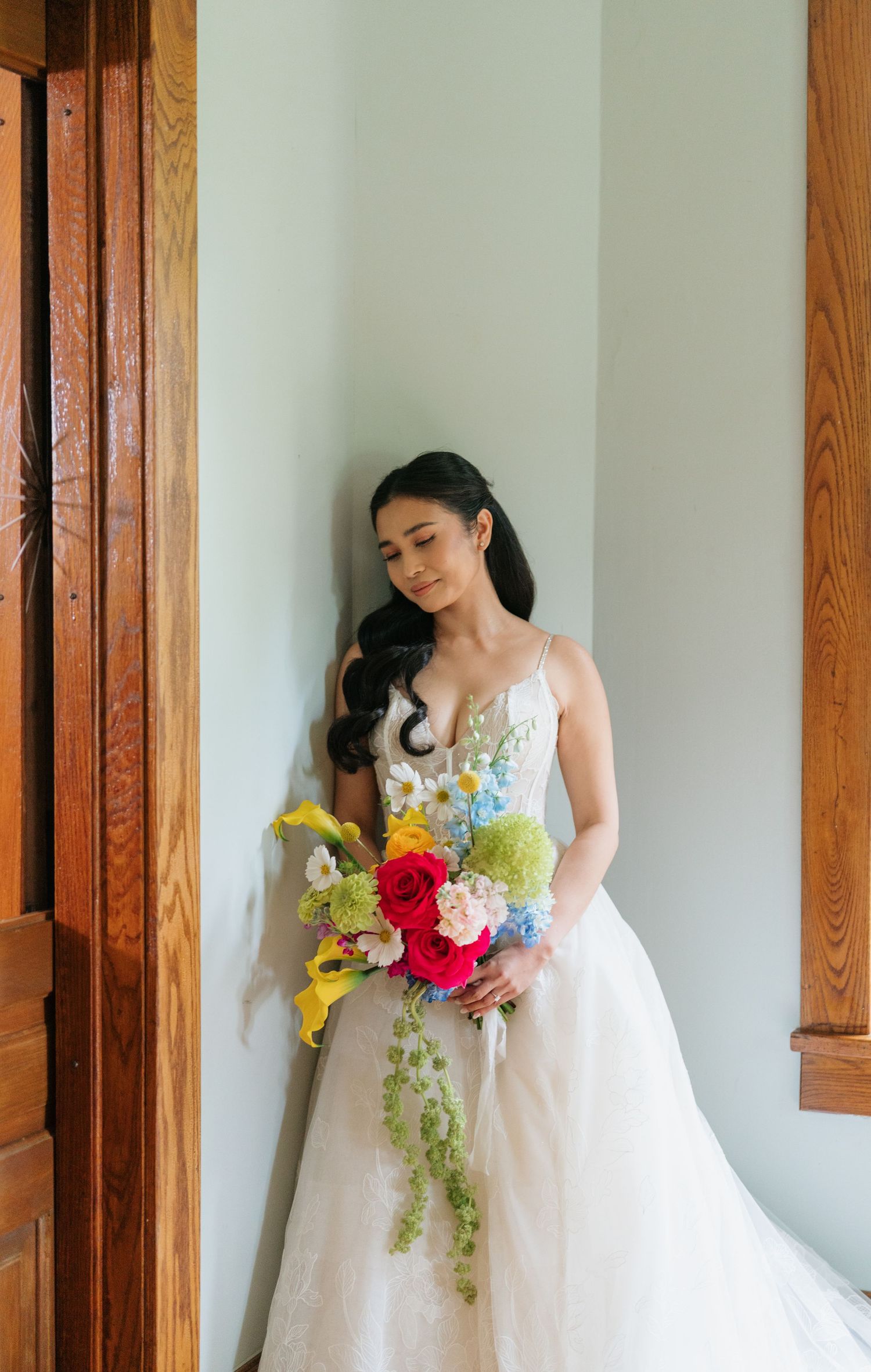 A bride in a white wedding gown holds a vibrant cascading bouquet with red, yellow and blue flowers.