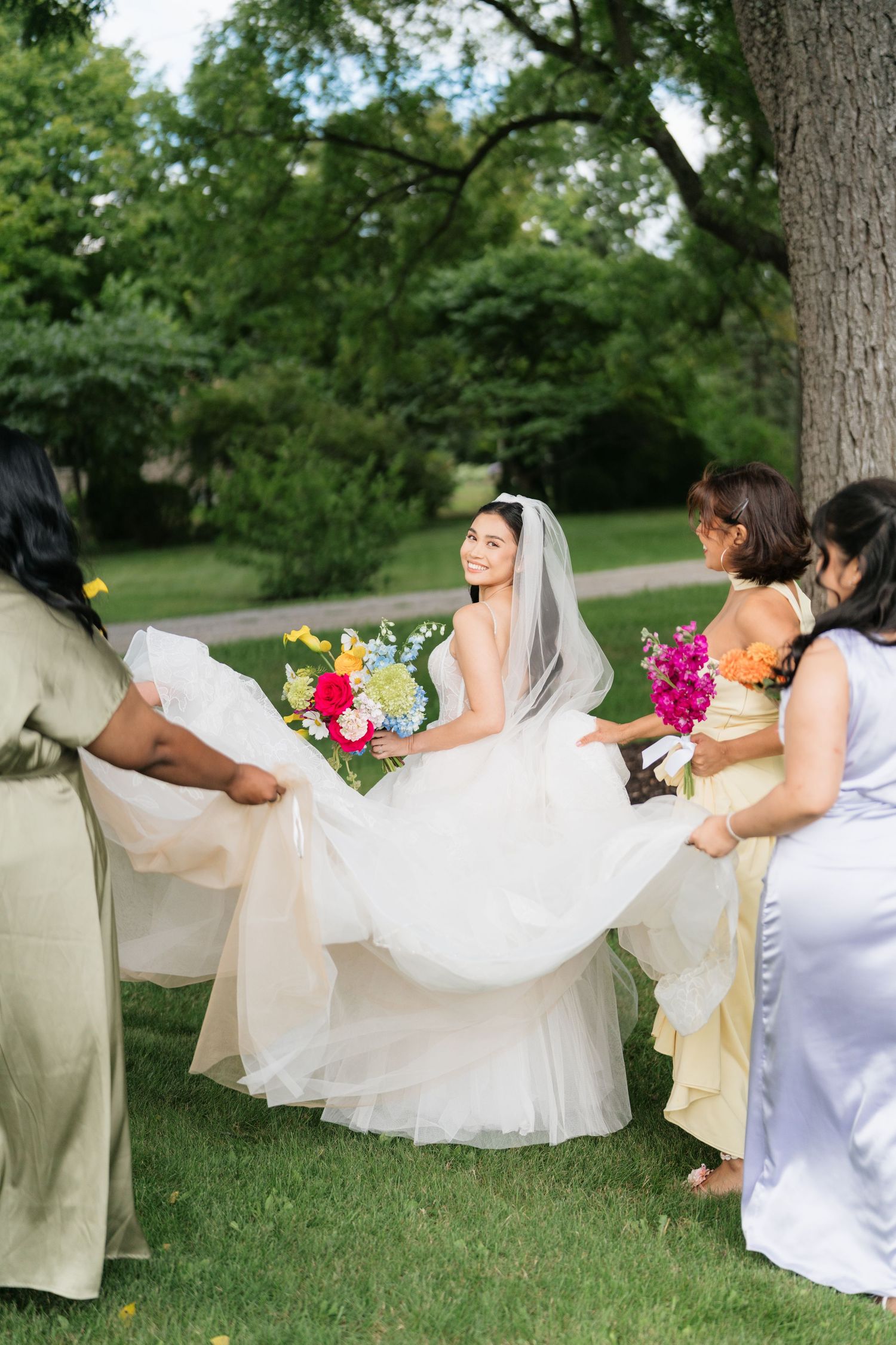 A series of photos showing a bride's flowing white dress and veil being lifted by the wind in a green outdoor setting.