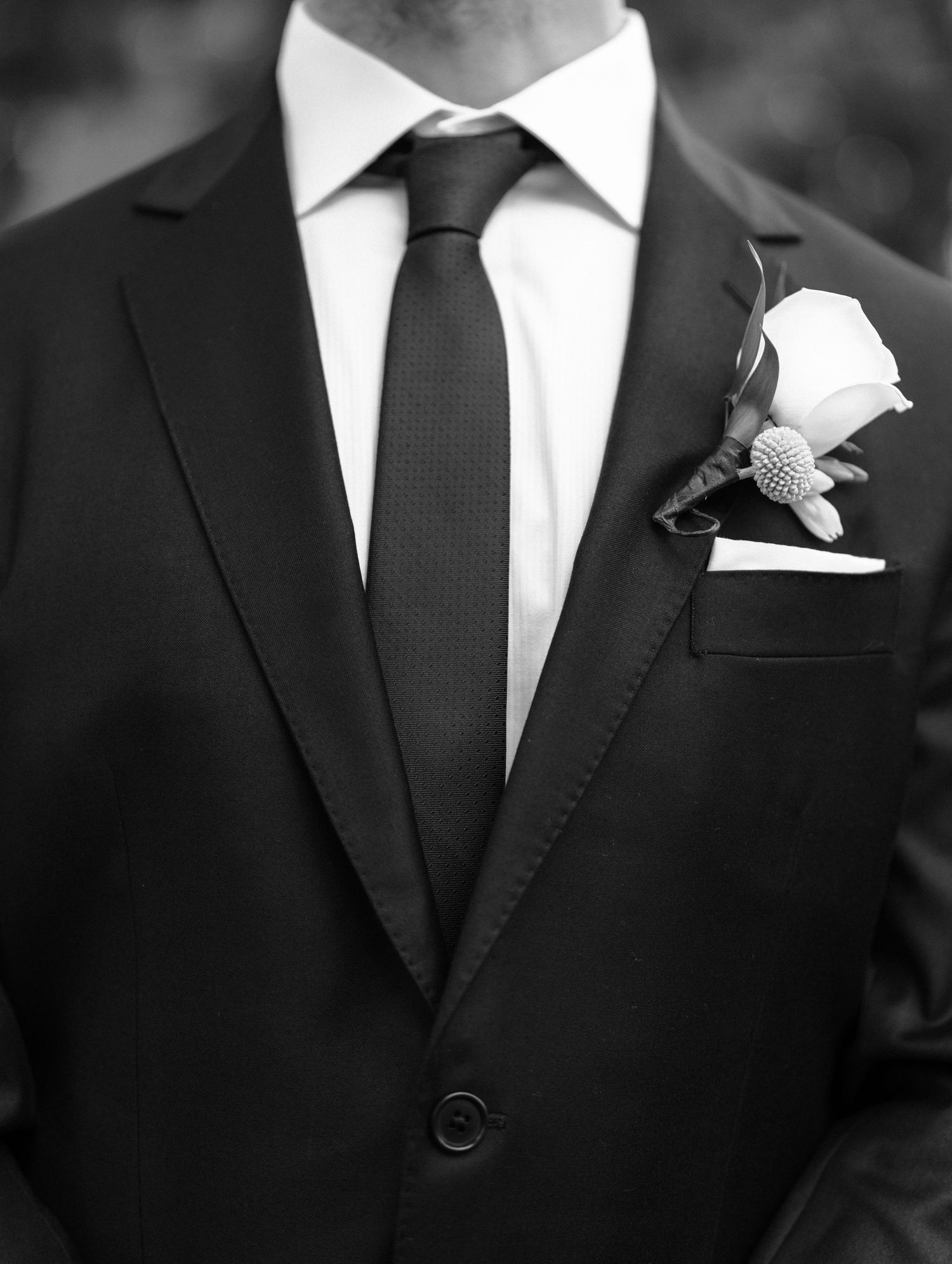 Close-up details of black tuxedos with white pocket squares and boutonniere flowers.