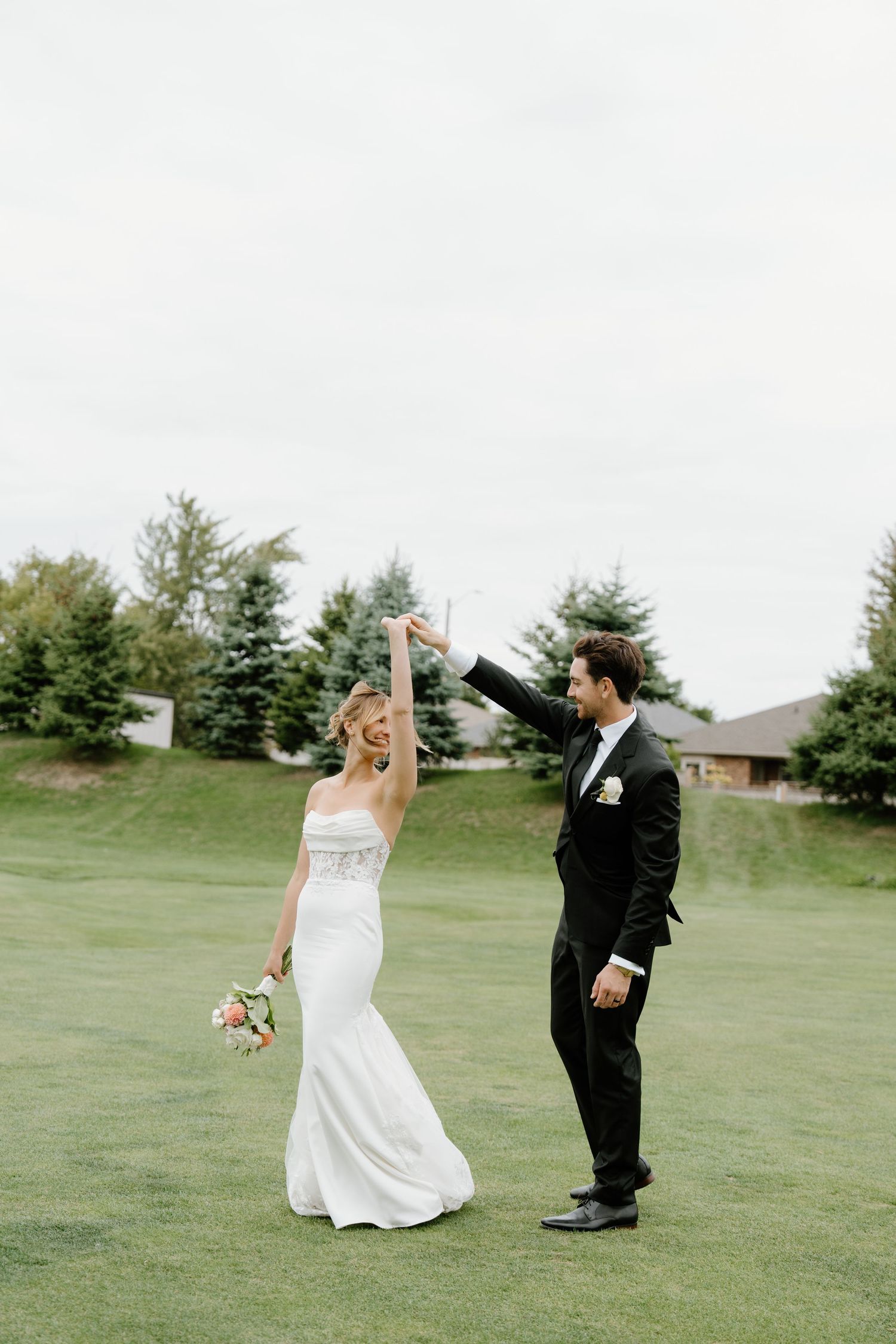 Newlywed couple dancing playfully on a grassy lawn during their wedding photoshoot.