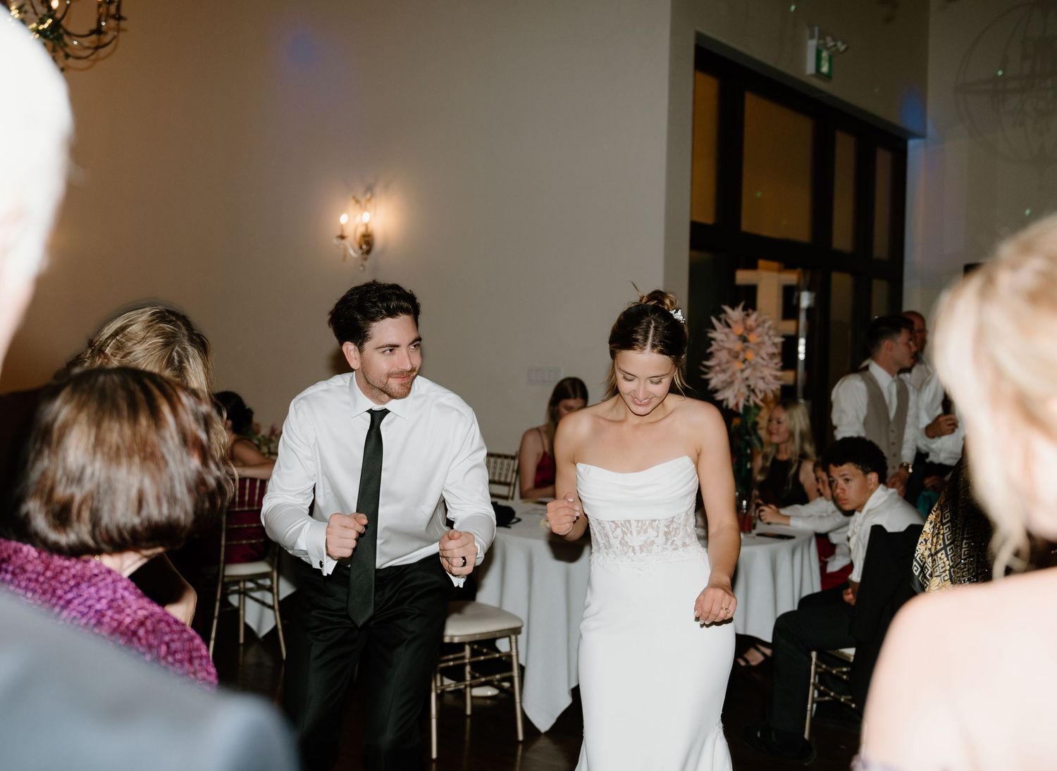 Wedding guests dance and celebrate together on a dimly lit dance floor during an evening reception.