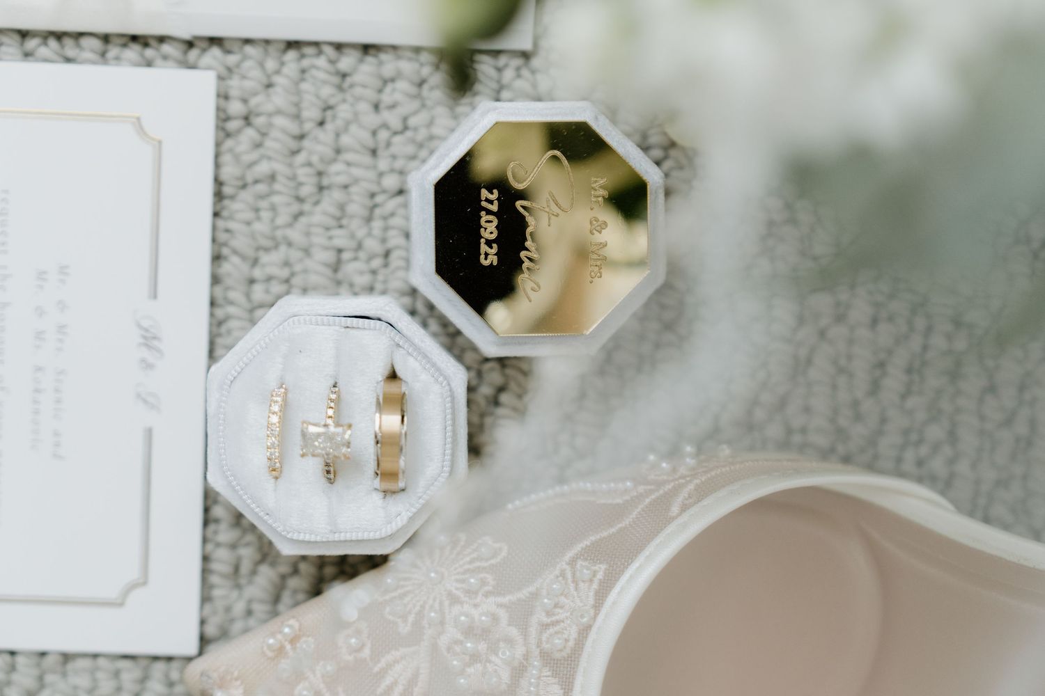 Wedding details including white invitation cards, rings, and delicate floral arrangements on a light gray surface.