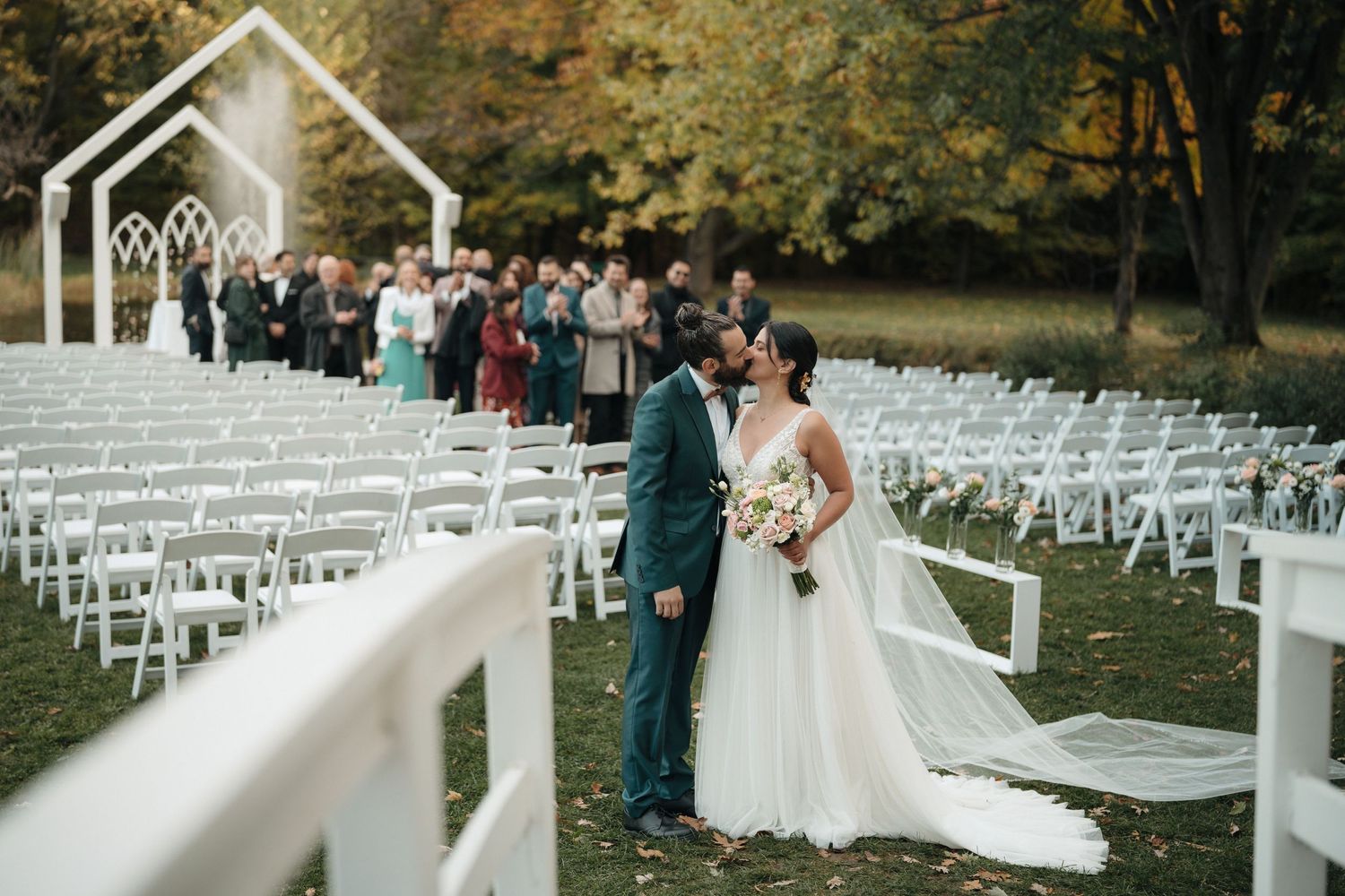 Outdoor wedding ceremony setup with white chapel and rows of chairs under autumn trees.