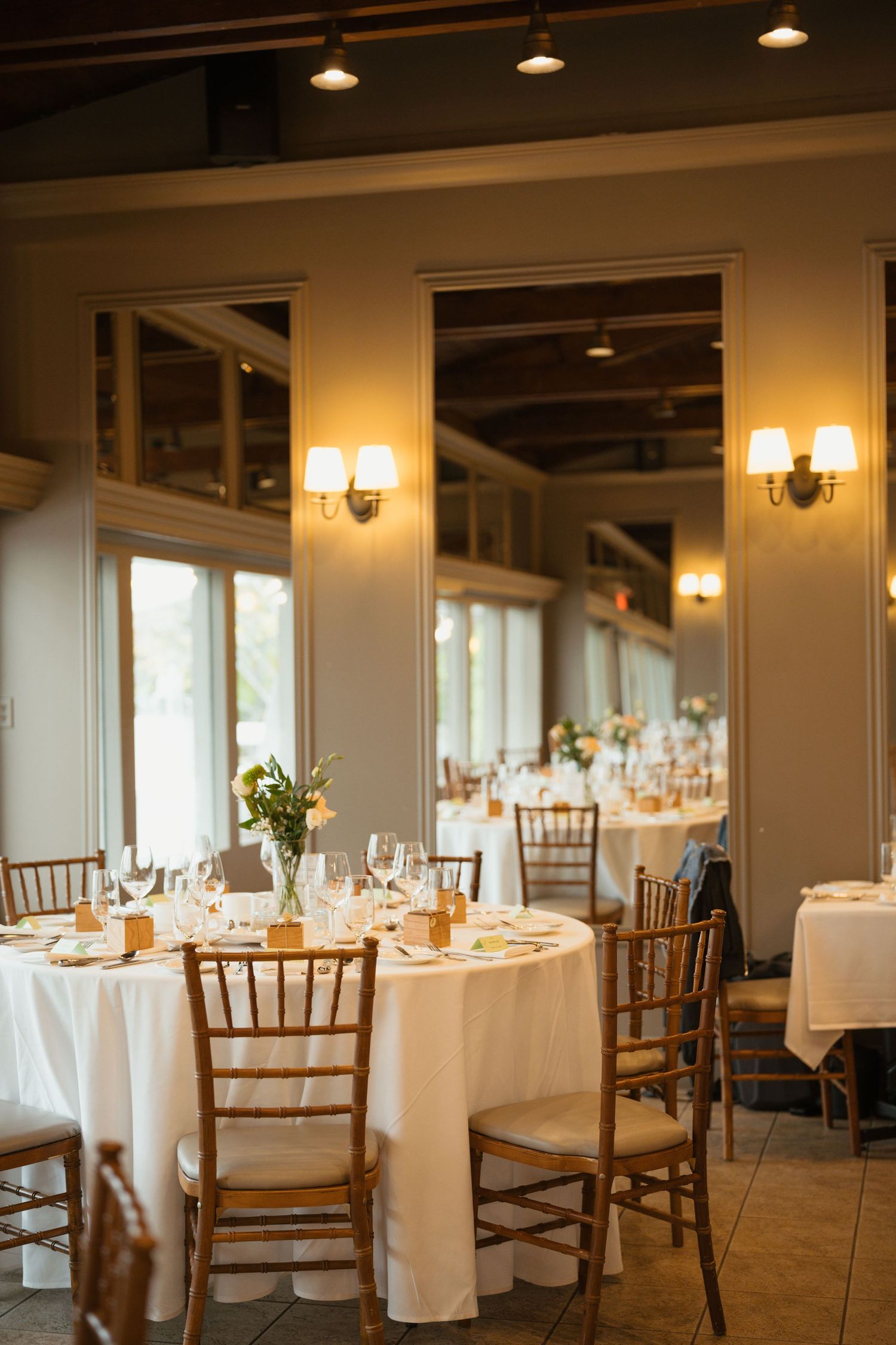 Wedding reception hall with wall sconces, white tablecloths, and warm ambient lighting.