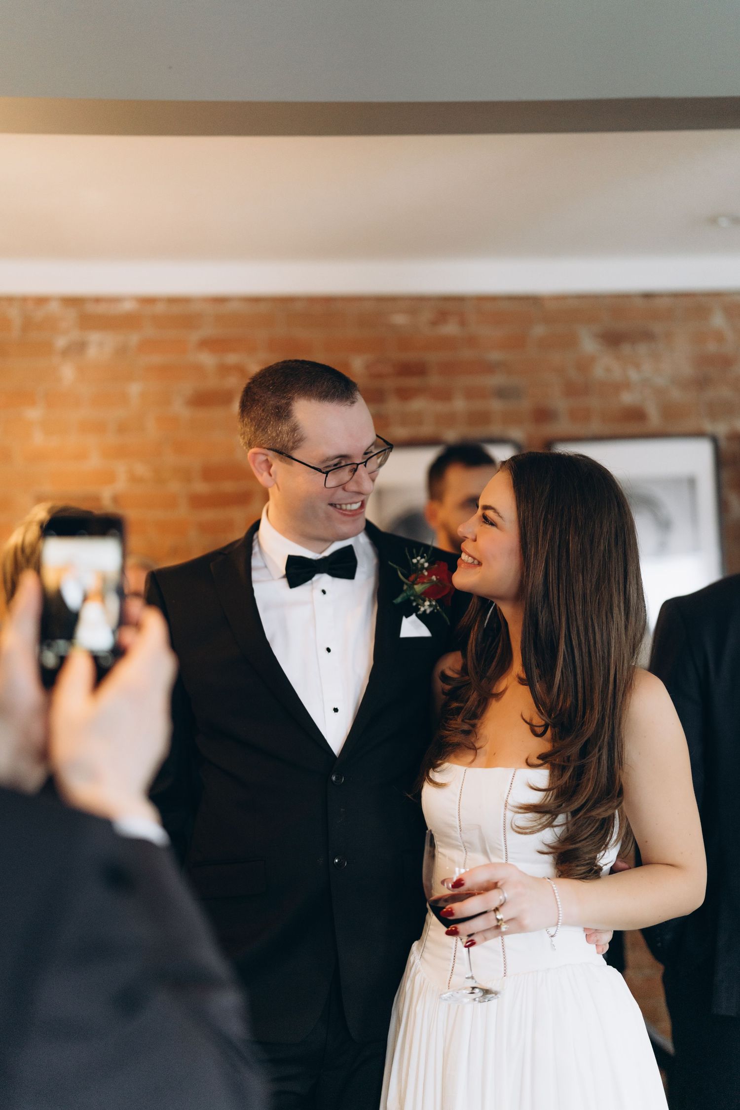 A joyful wedding moment captured as someone takes a photo on their phone of a couple in formal attire.