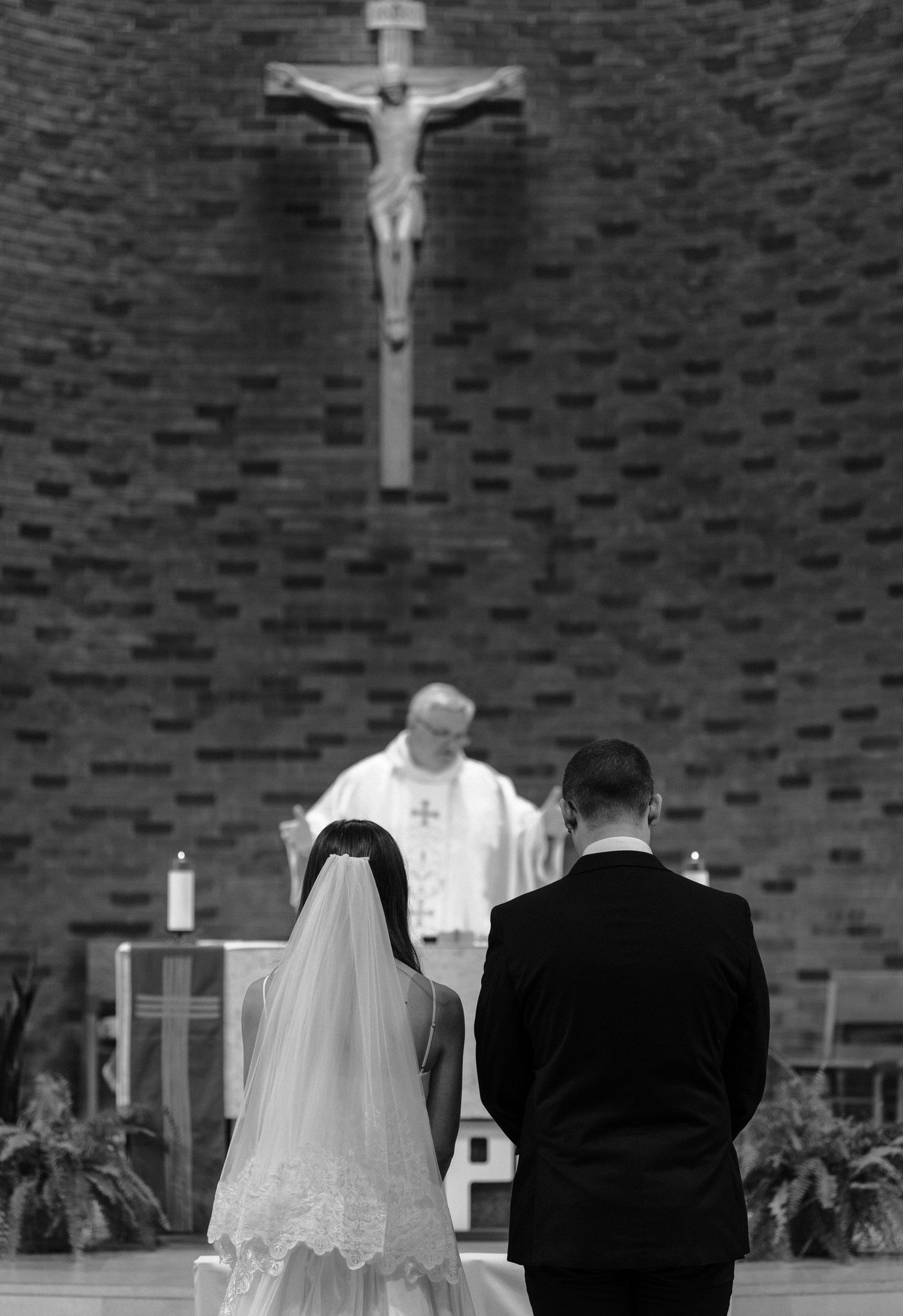 Wedding ceremony scene in a church with a crucifix on a brick wall behind the couple.