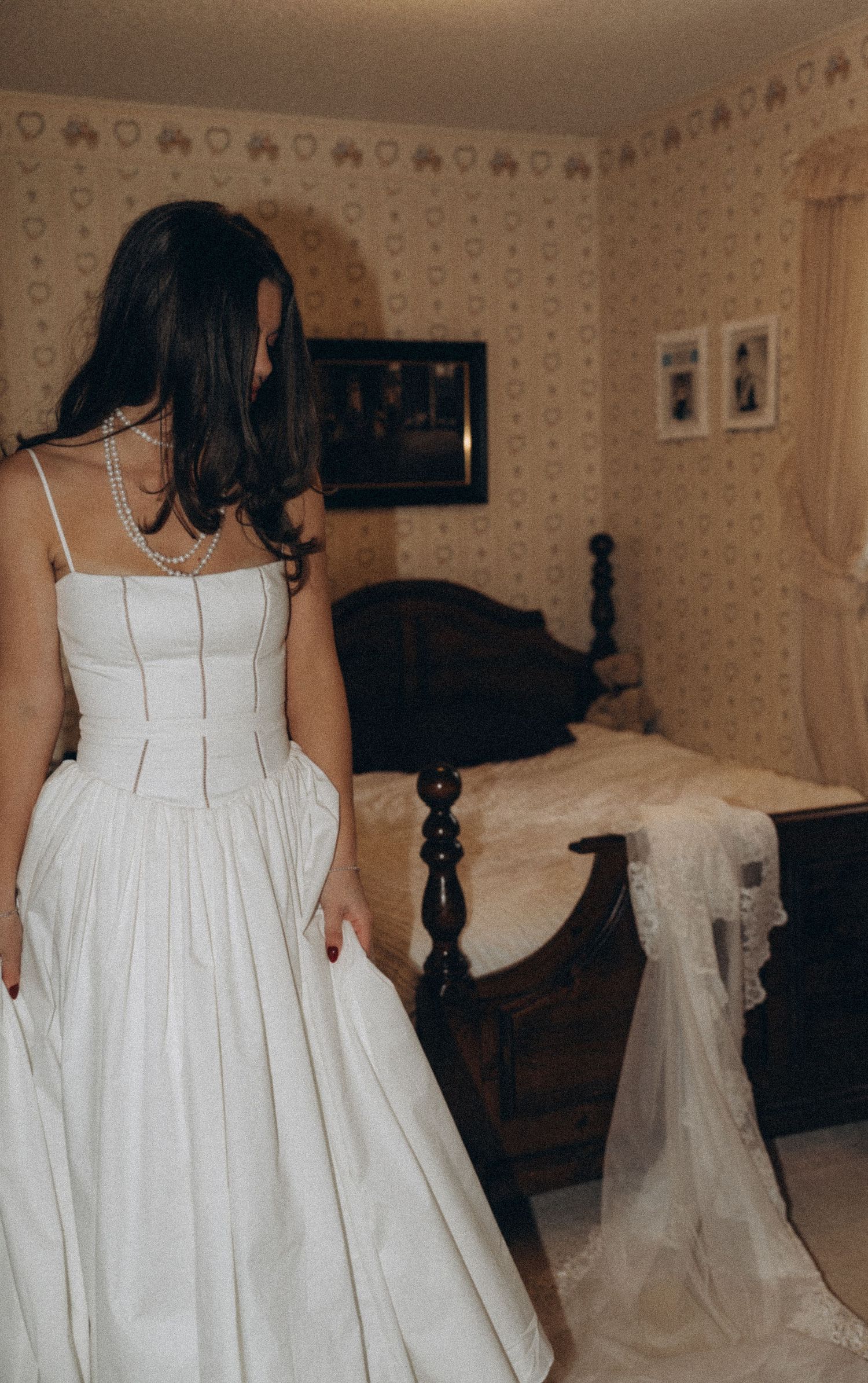 Back view of someone wearing a white wedding dress with corset detail in a vintage-styled room with floral wallpaper.