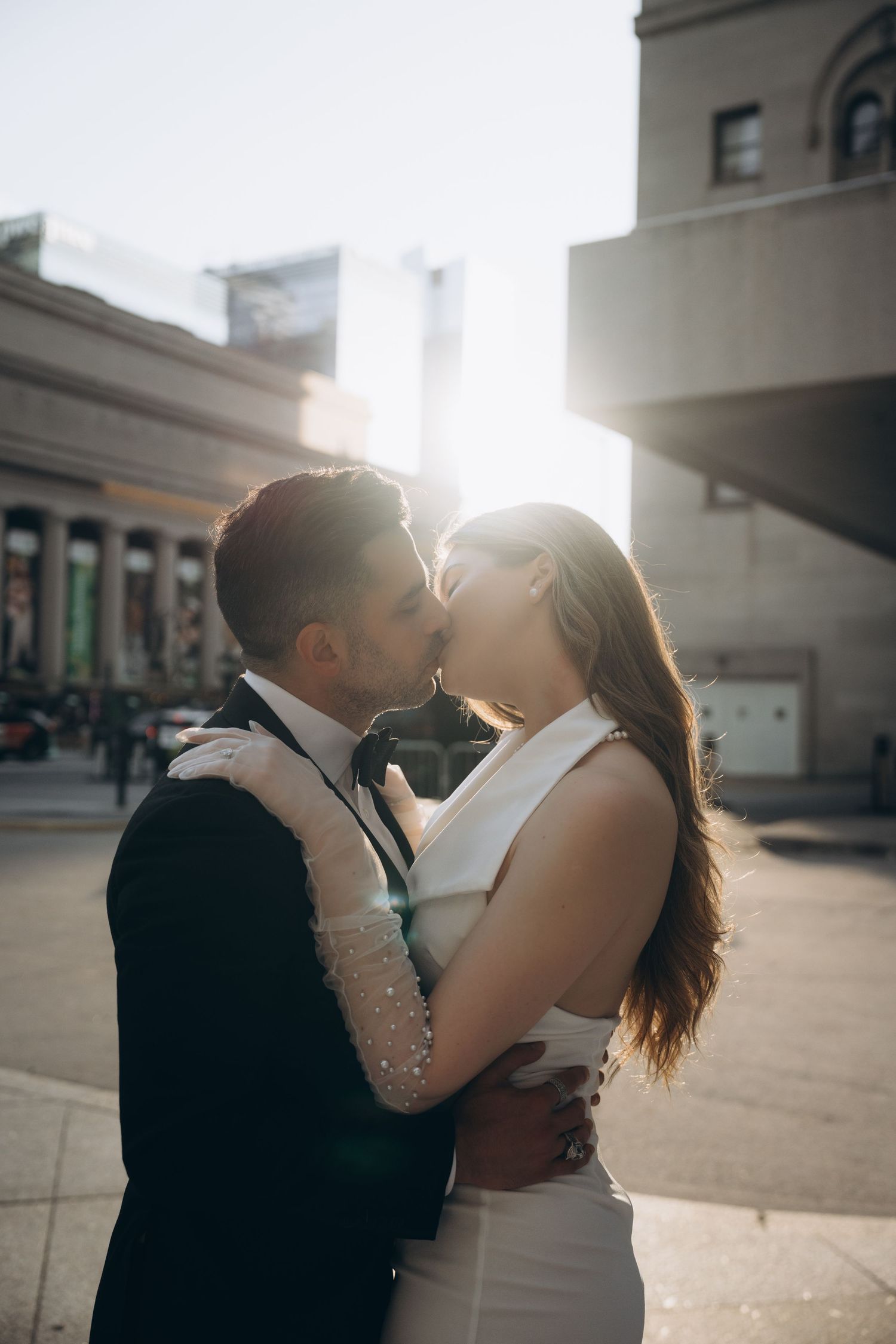 A romantic couple embraces and kisses in silhouette against bright sunlight on an urban rooftop.