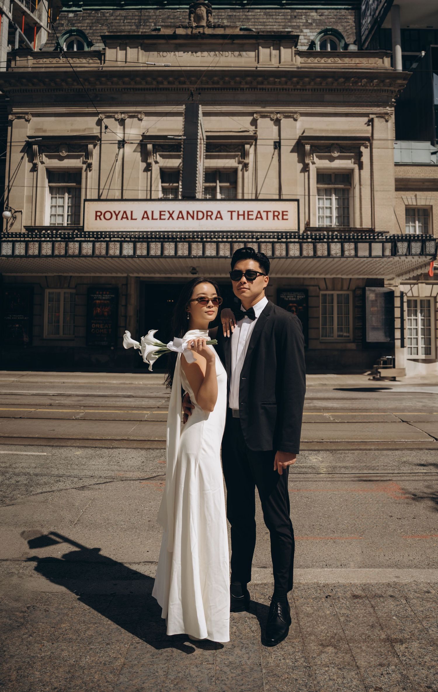 A couple in formal attire poses outside the historic Royal Alexandra Theatre's elegant facade.