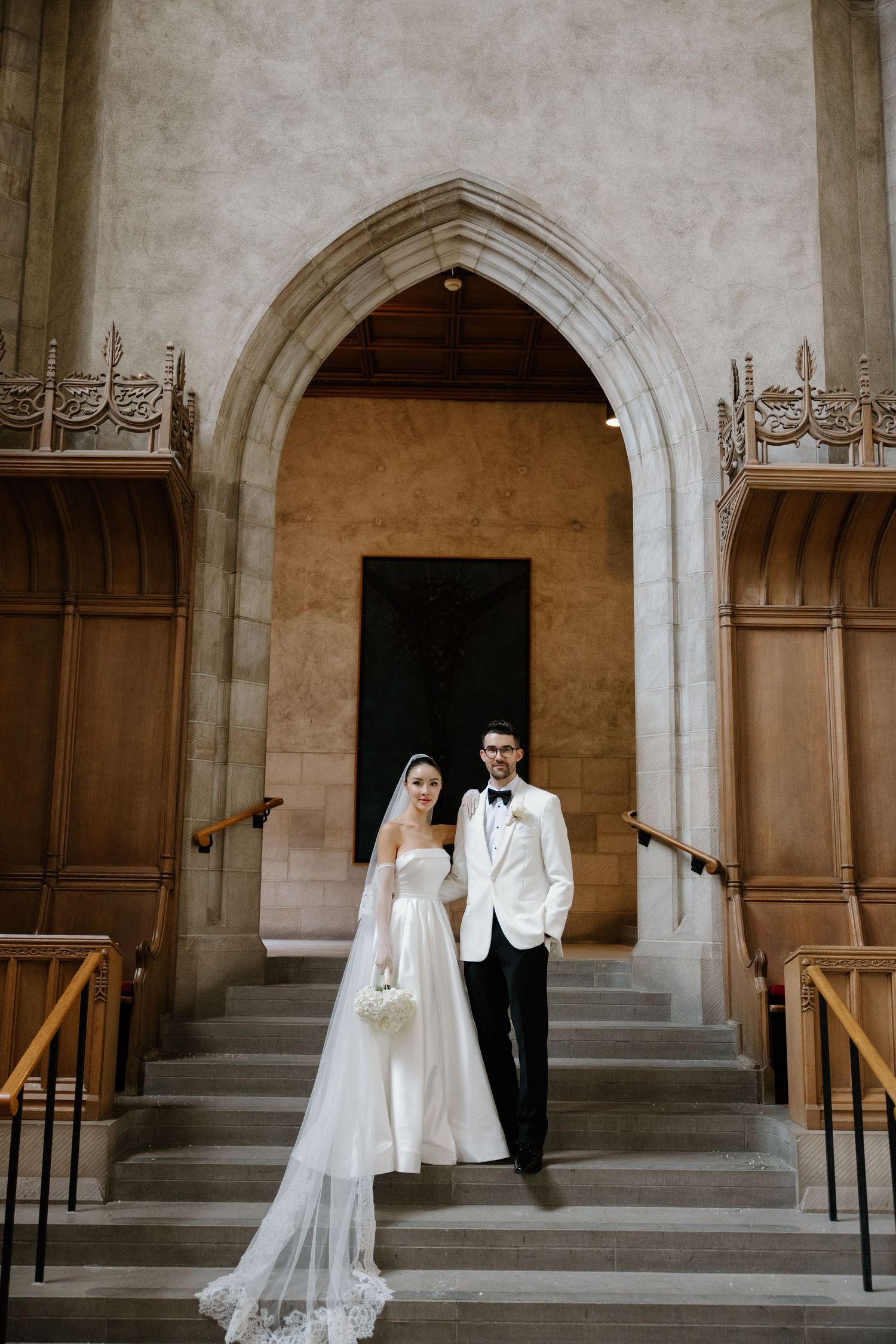 Elegant wedding couple stands in a Gothic church doorway with arched entrance and ornate wooden interior details.