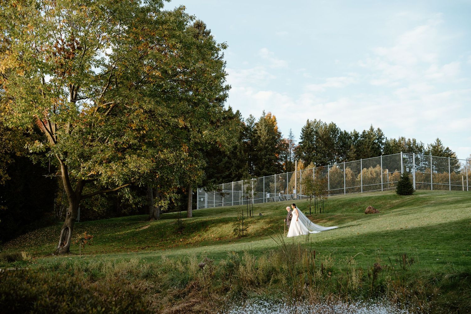White arched structure on a hillside with autumn trees and fencing in the background.