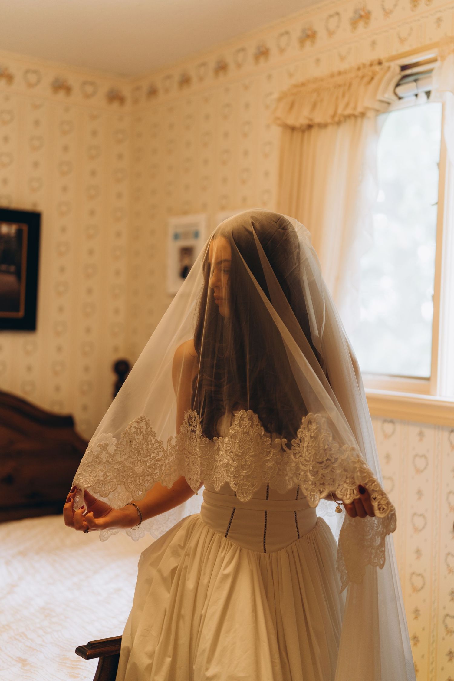 Back view of bride in wedding dress and veil moving through a room with floral wallpaper.