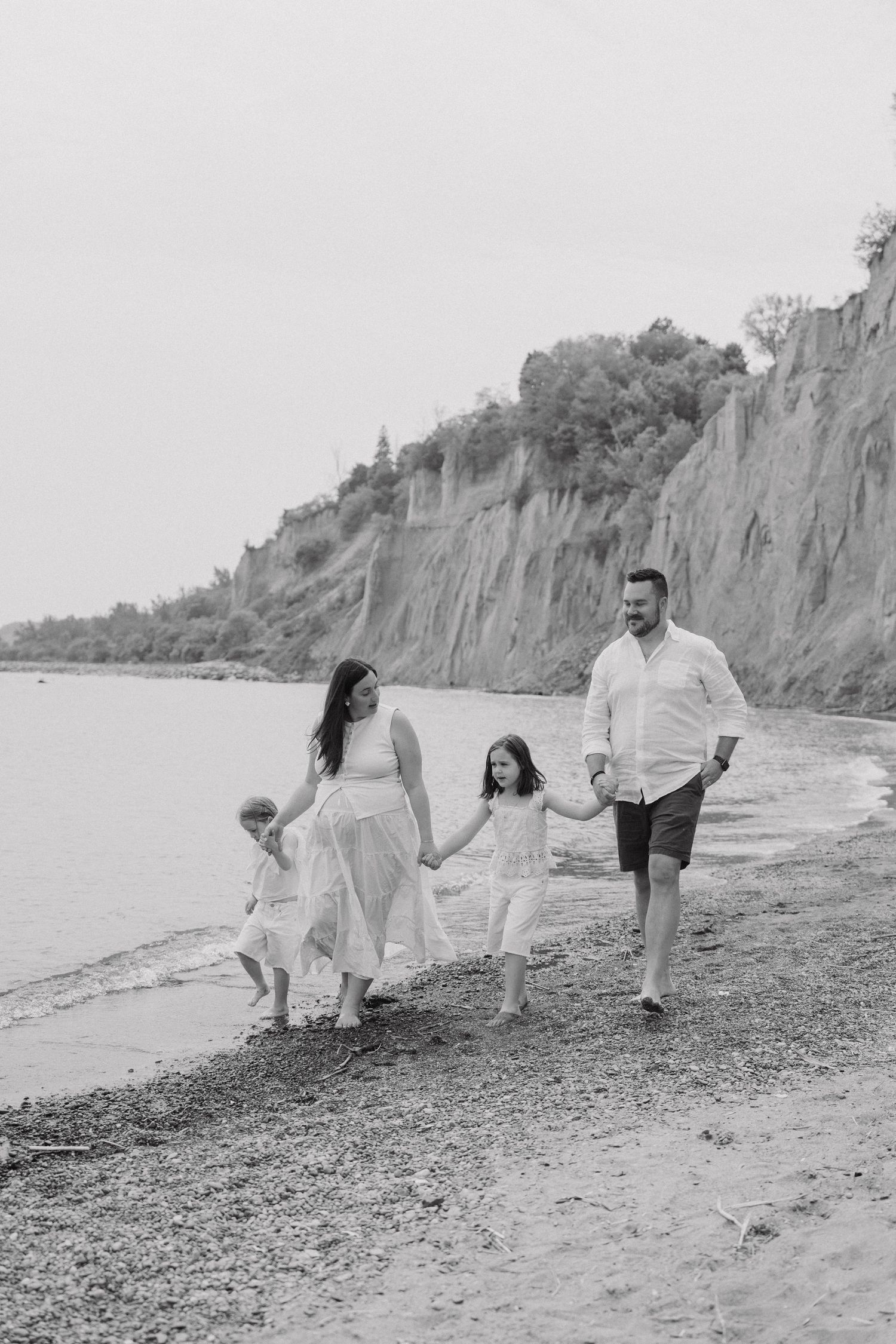A black and white photo sequence shows a family joyfully playing and running together along a rocky beach shoreline.