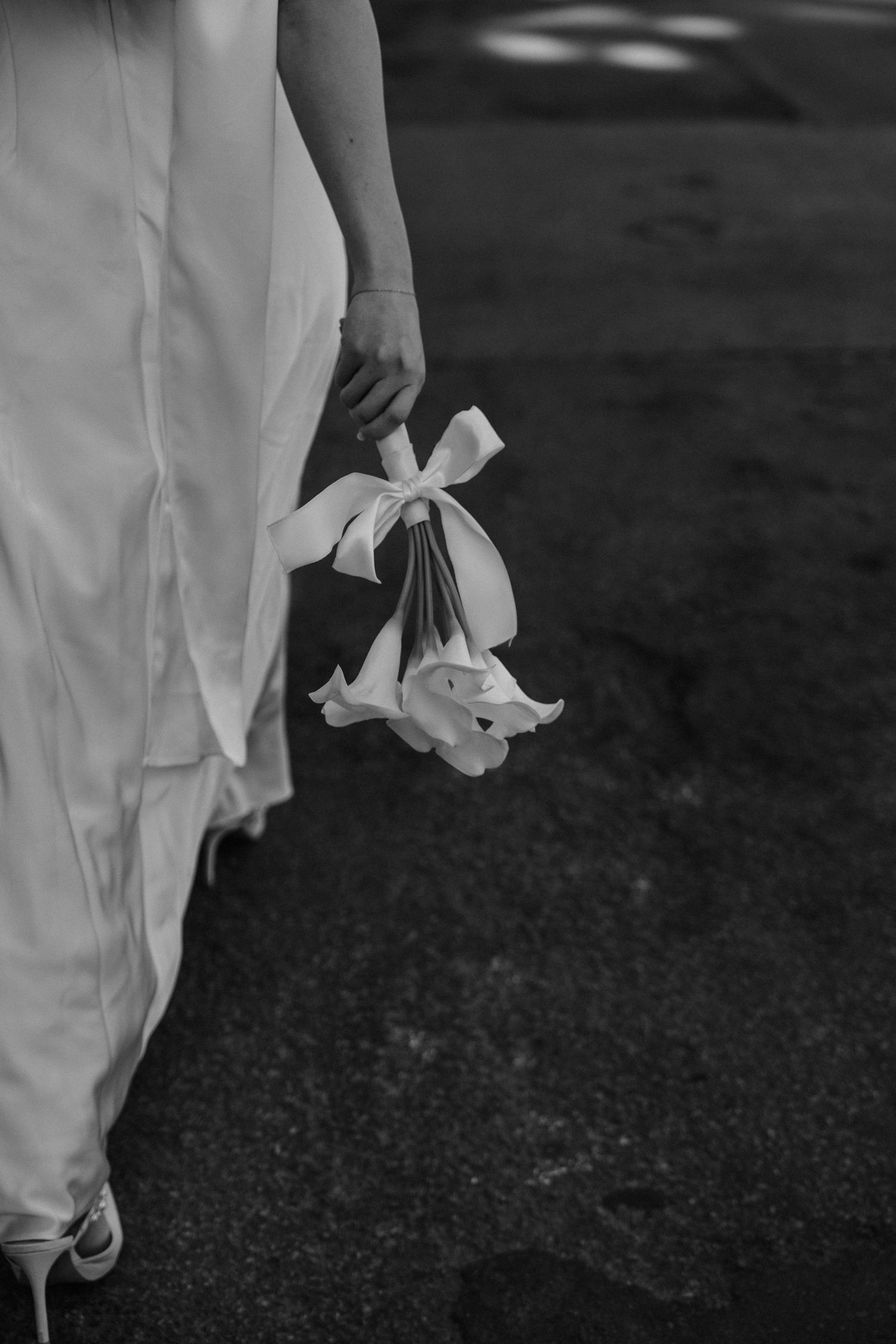 Black and white image of someone in a white dress holding a small stuffed animal with a bow attached to it.