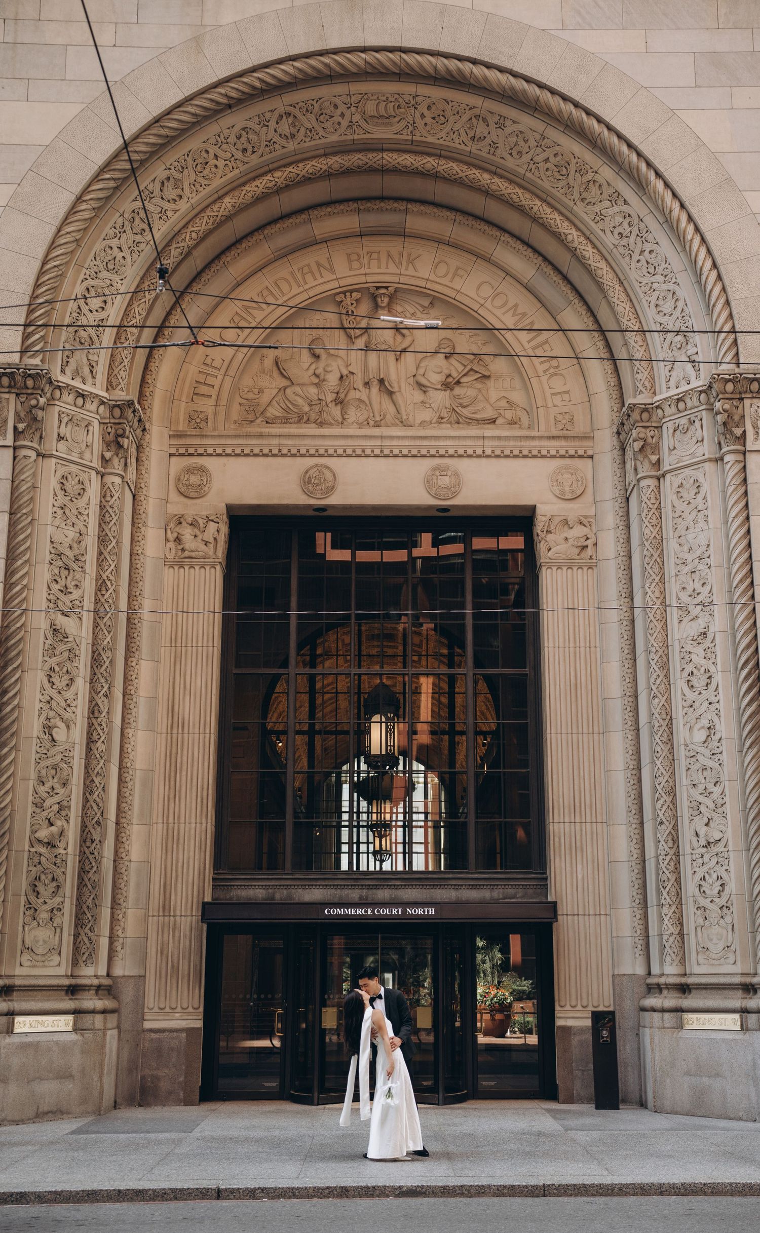 A bride stands under an elaborately carved stone archway entrance with decorative columns and religious motifs.