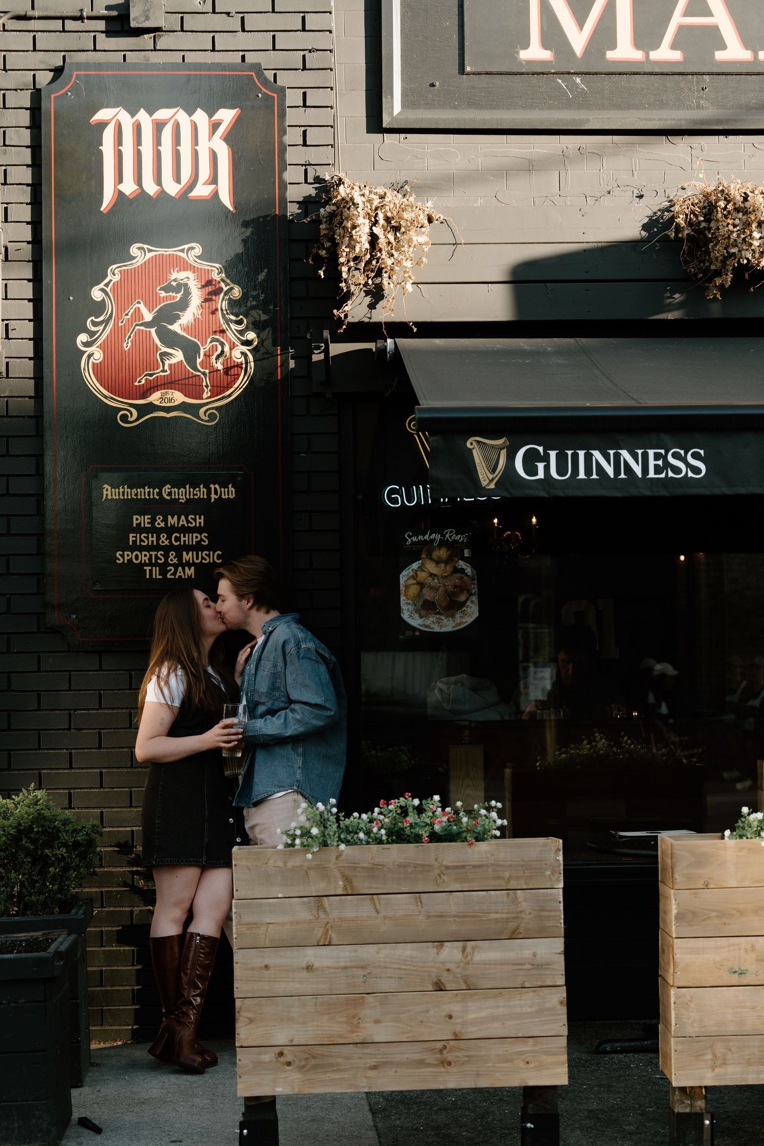 A cozy exterior of a pub with wooden planters and signage showing Guinness beer branding on a brick wall.