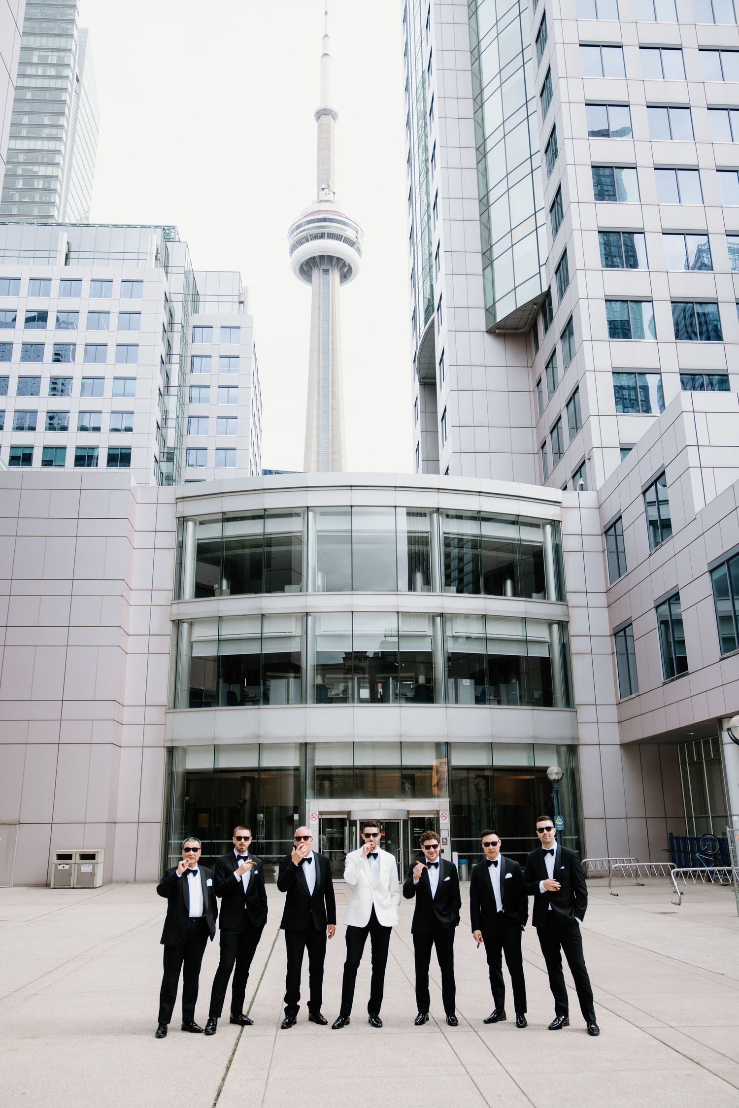 A wedding party stands in front of modern glass buildings and the CN Tower in downtown Toronto.
