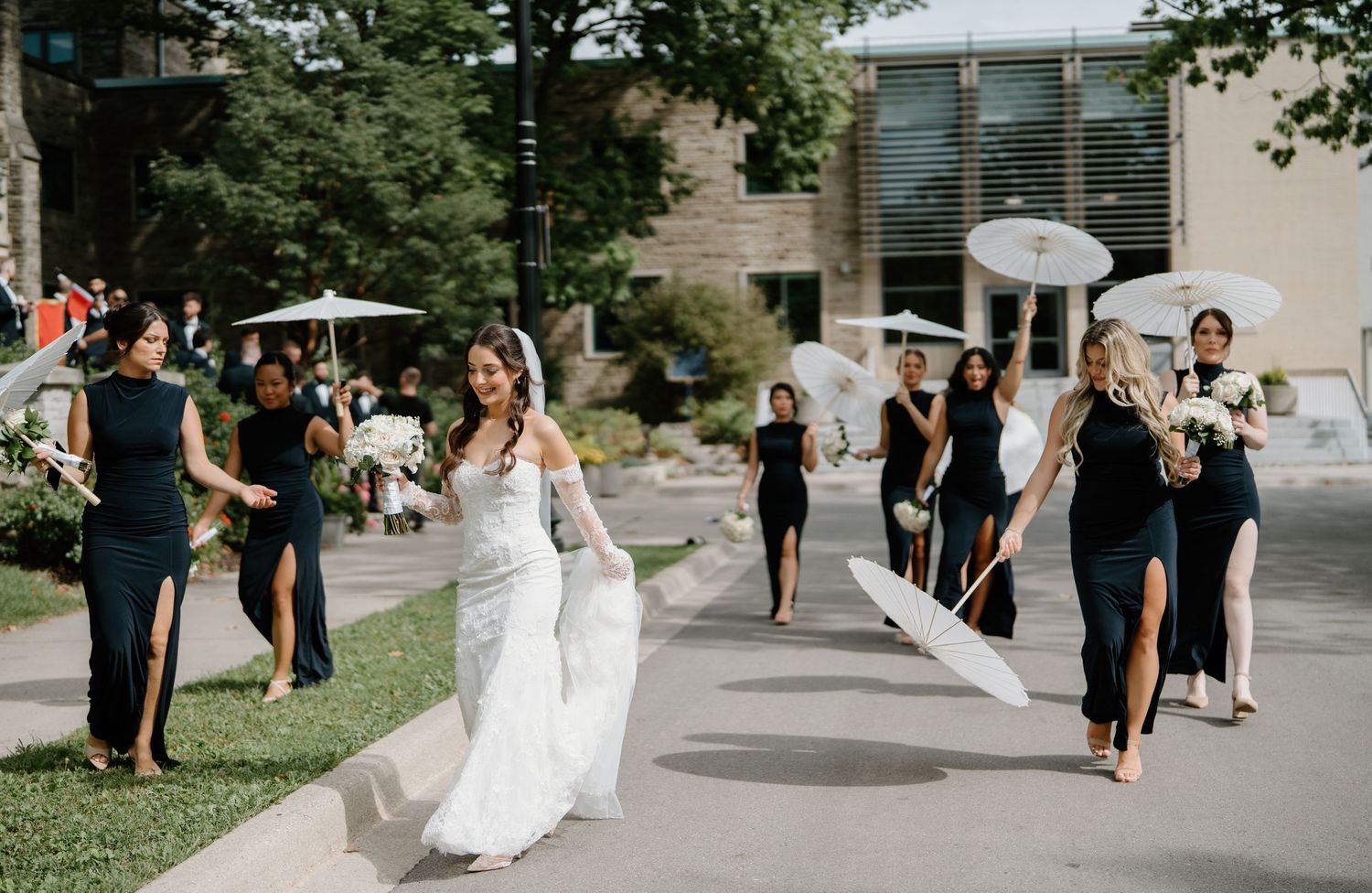 A joyful wedding celebration outdoors with a flowing white bridal gown and attendants in dark dresses.