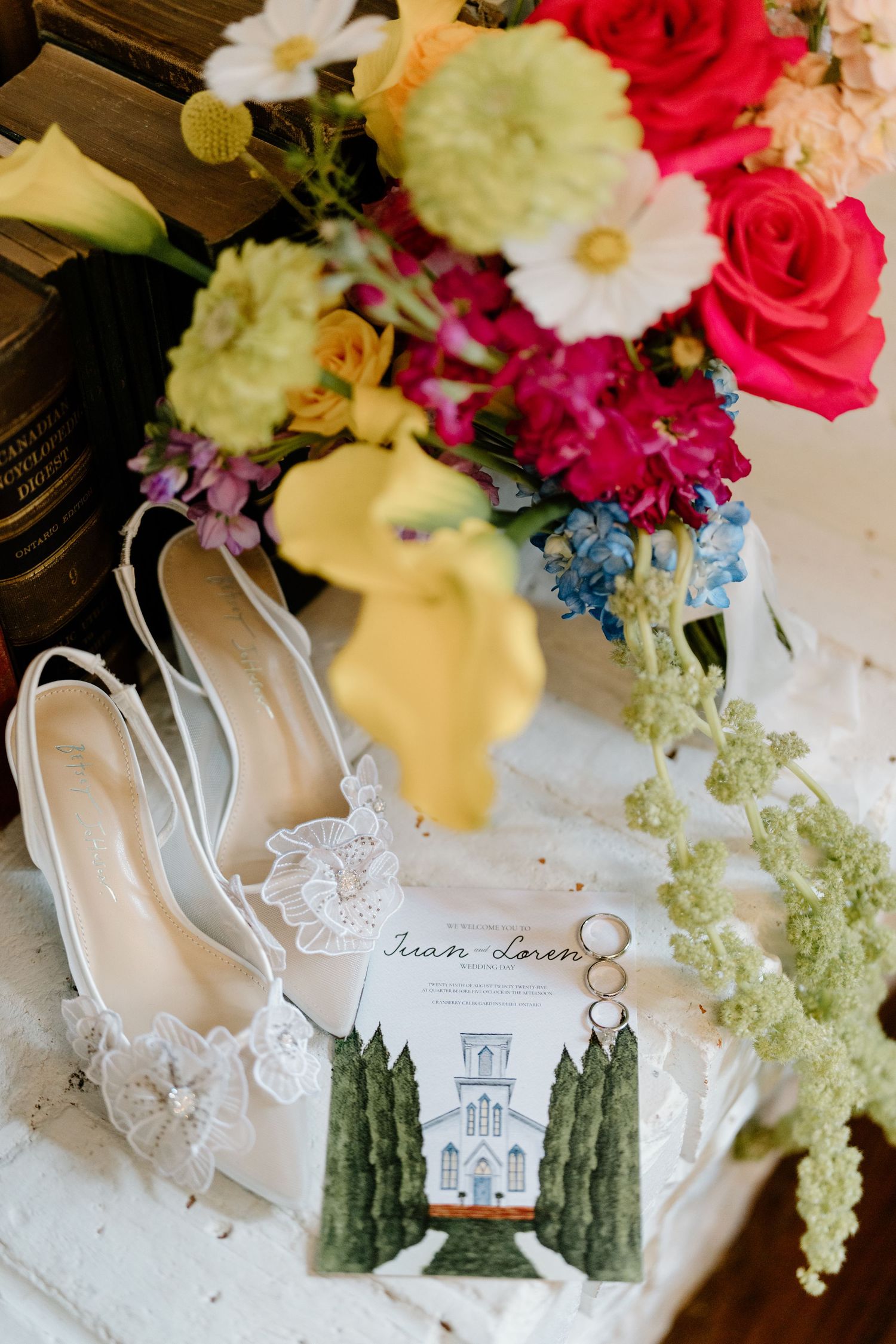 Colorful floral wedding centerpiece with pink roses and white flowers arranged on lace doily with illustrated venue card.