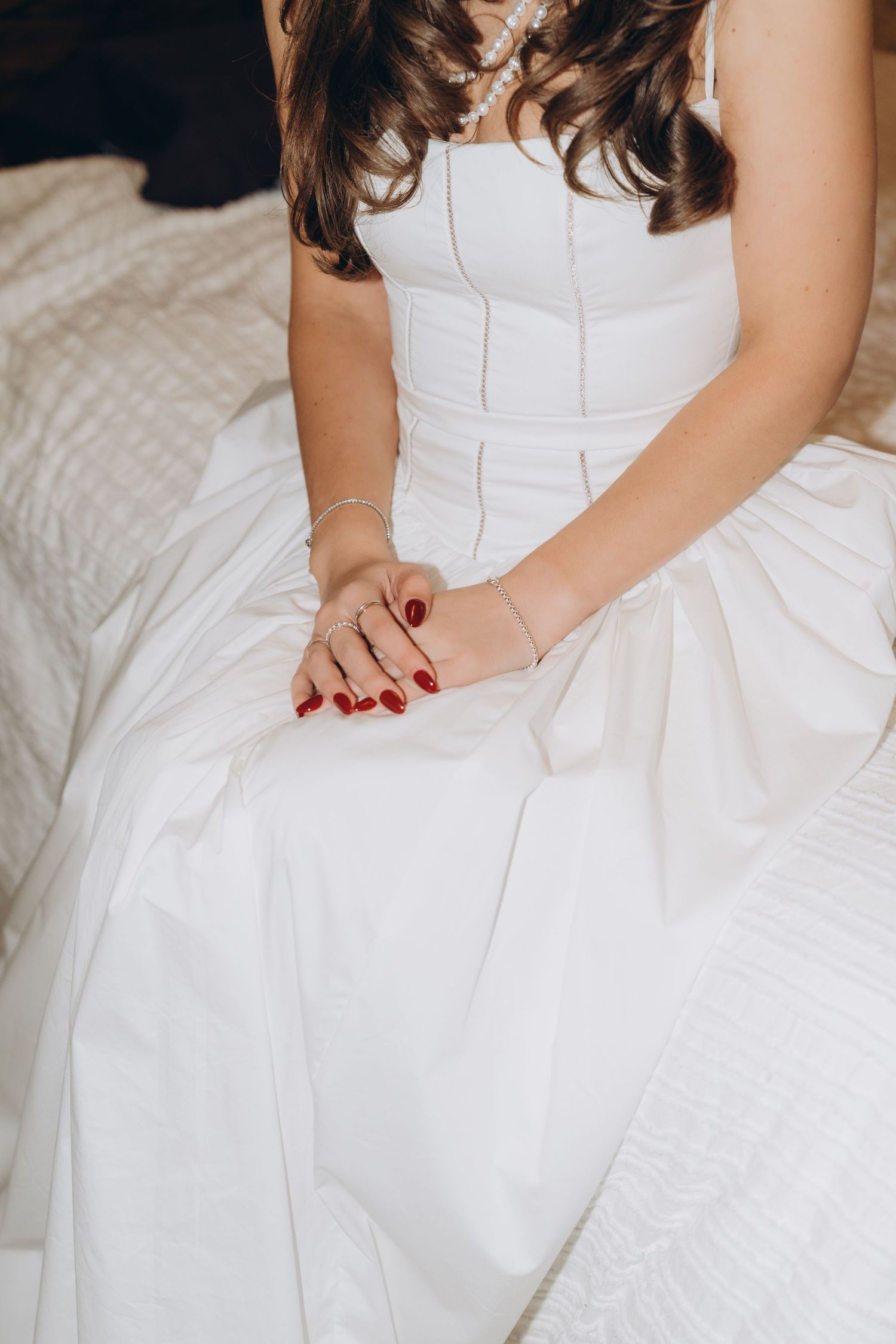 Close-up of a person in a white wedding dress with red nail polish resting their hands on their lap.