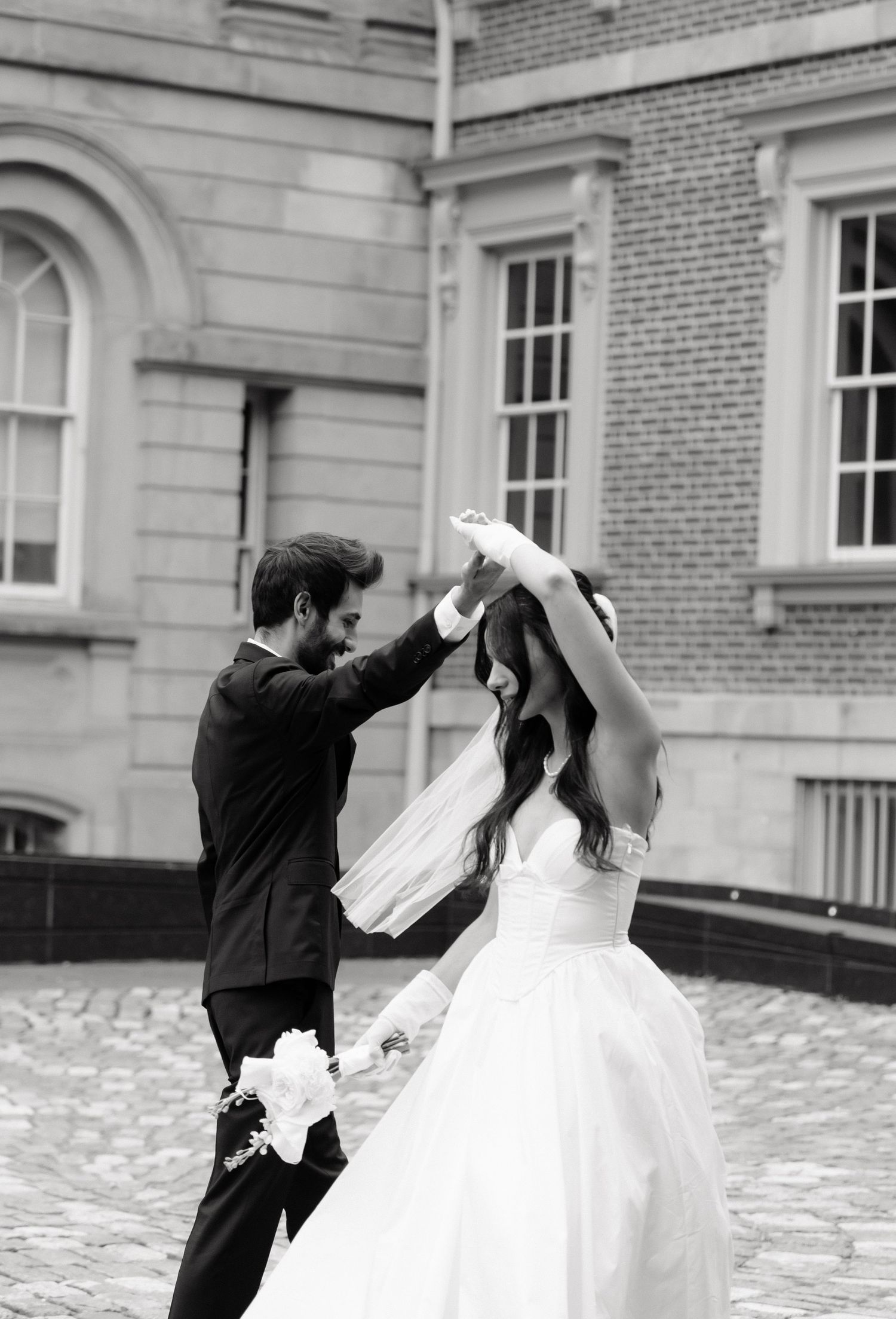 A black and white photo sequence shows a couple in wedding attire dancing playfully on a brick courtyard.