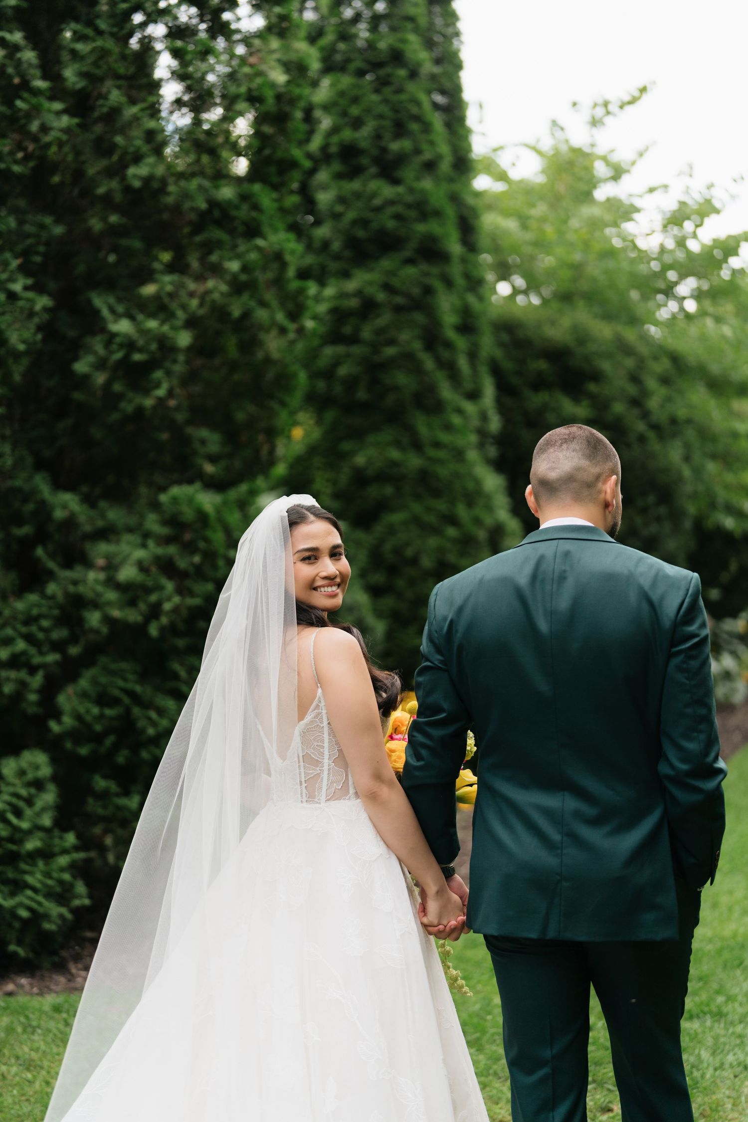 A couple walking together outdoors, with the bride wearing a flowing white veil and gown on their wedding day.