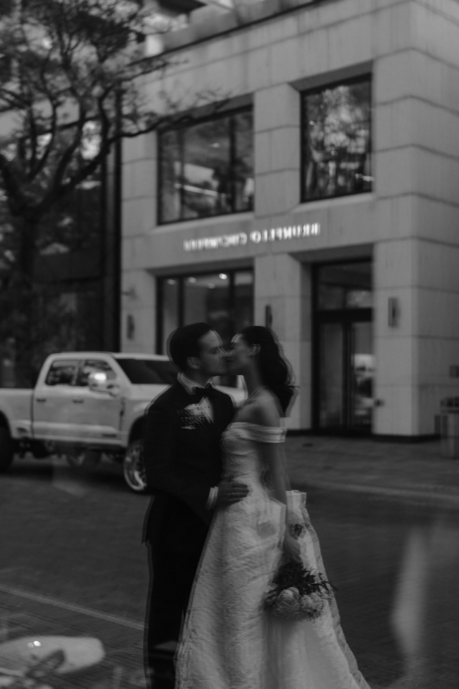 A romantic black and white photo series showing a couple dancing together on a city sidewalk at dusk.