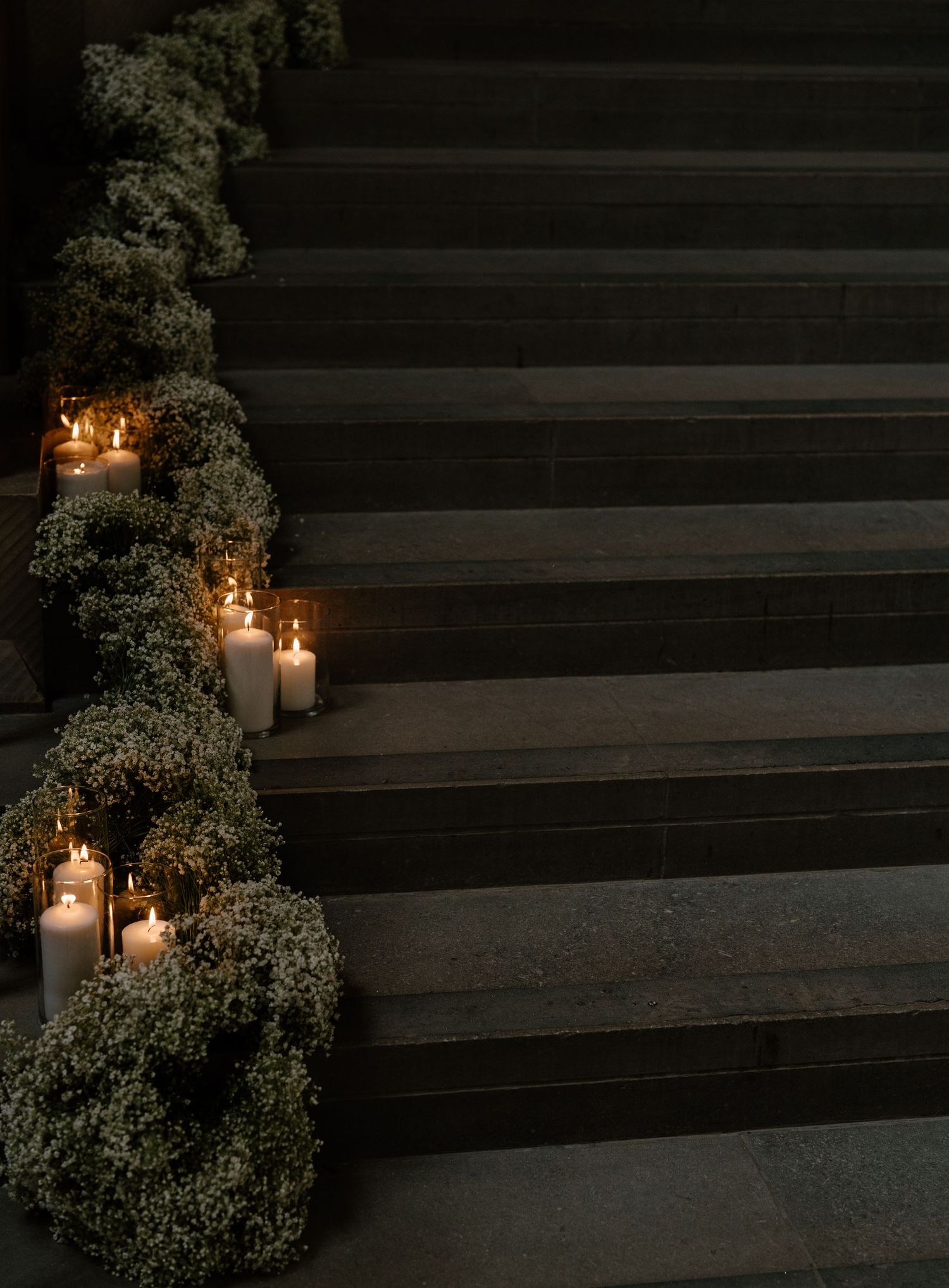 Dark stone steps decorated with glowing candles and lush greenery creating romantic wedding ambiance.