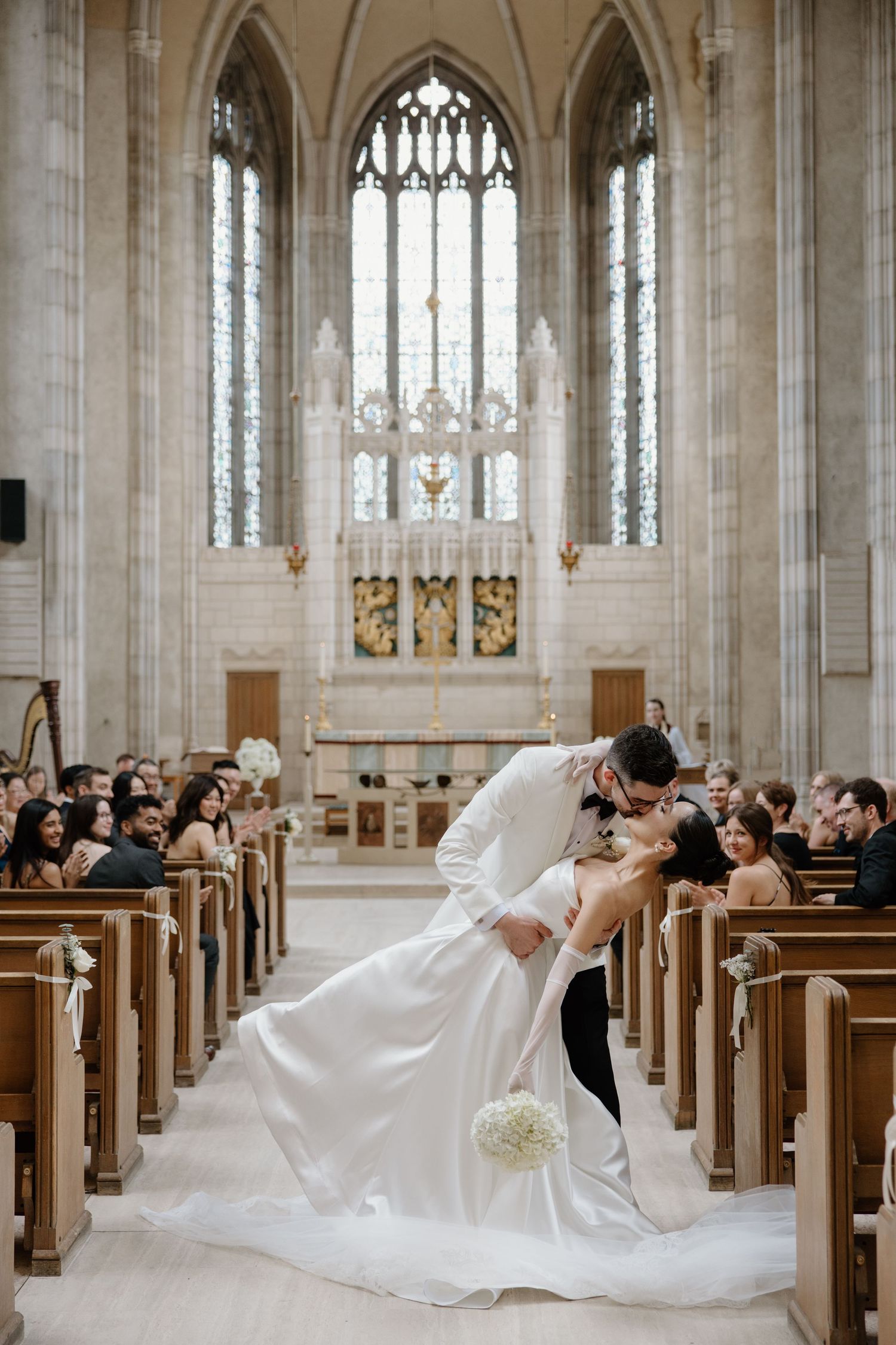 A romantic wedding moment captured inside a grand Gothic church with elegant stained glass windows and wooden pews.