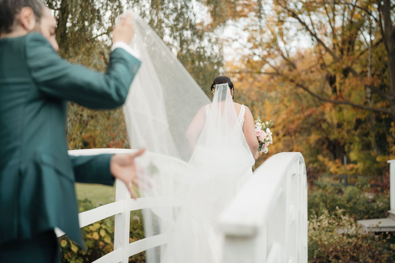 Close-up of flowing white wedding veil being held up against autumn trees.