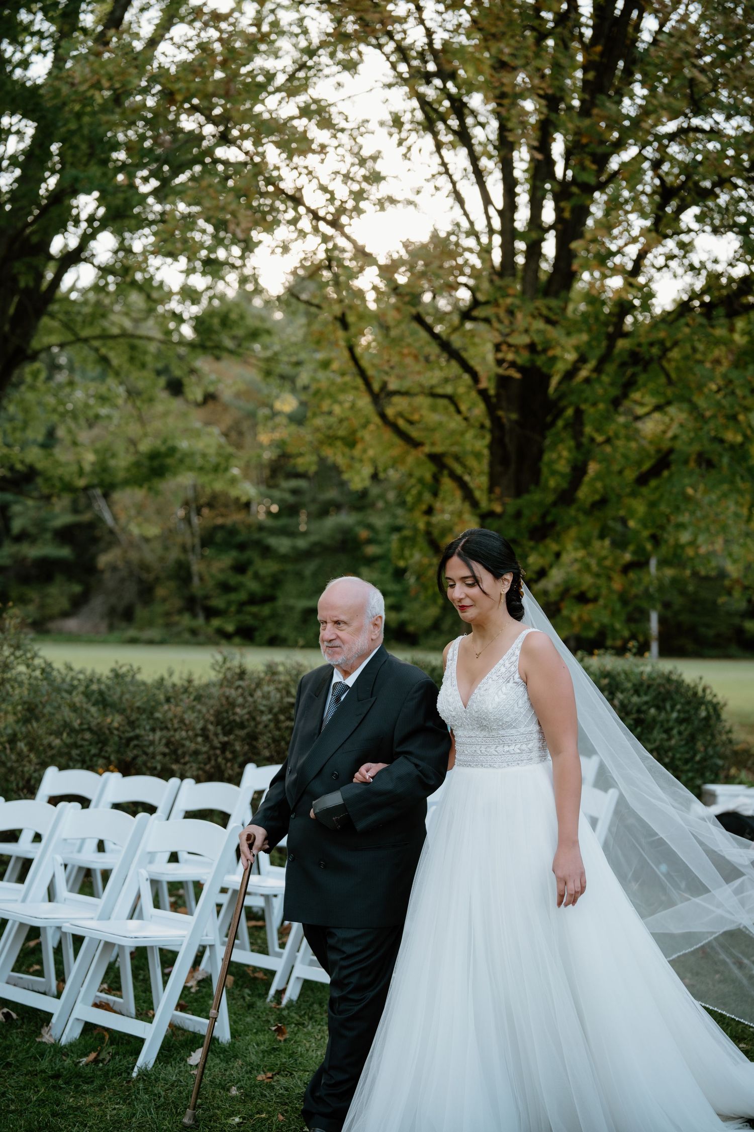 A formal processional moment captured on a lawn with white chairs set up for an outdoor wedding.