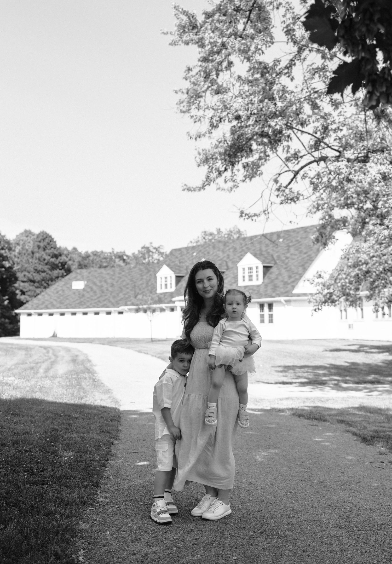 A black and white photograph shows two figures embracing on a lawn in front of a white colonial-style building with dormers.
