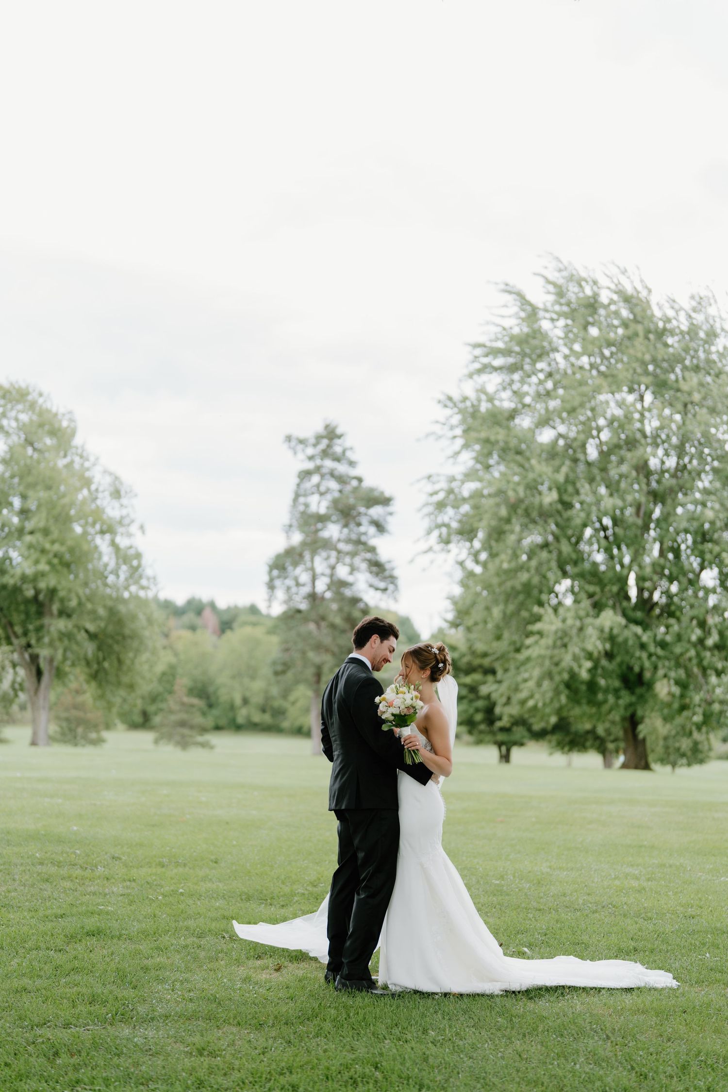 Elegant wedding couple embracing on a lush green lawn during an outdoor photoshoot.