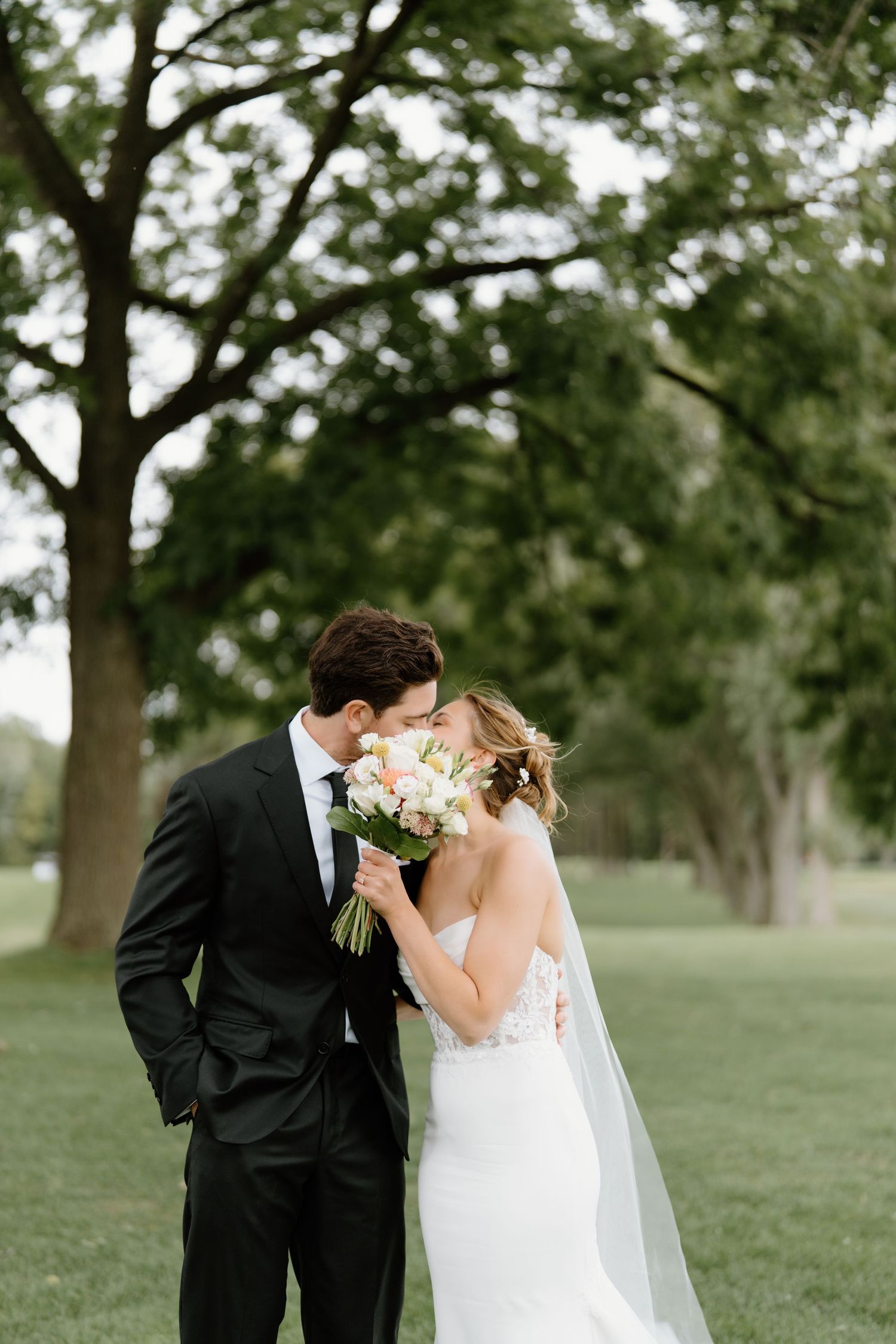 A romantic wedding couple shares an intimate moment with a bouquet in a lush garden setting.