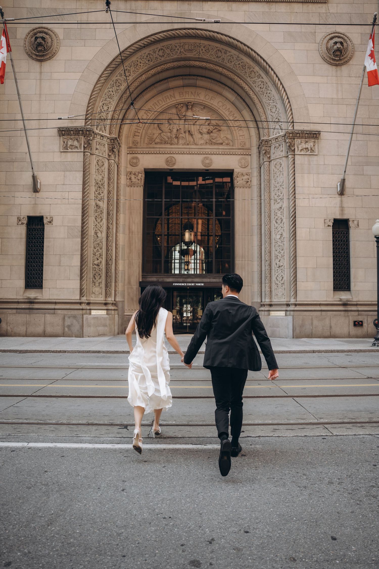 A couple walks towards an ornate arched entrance of a historic stone building with classical architectural details.