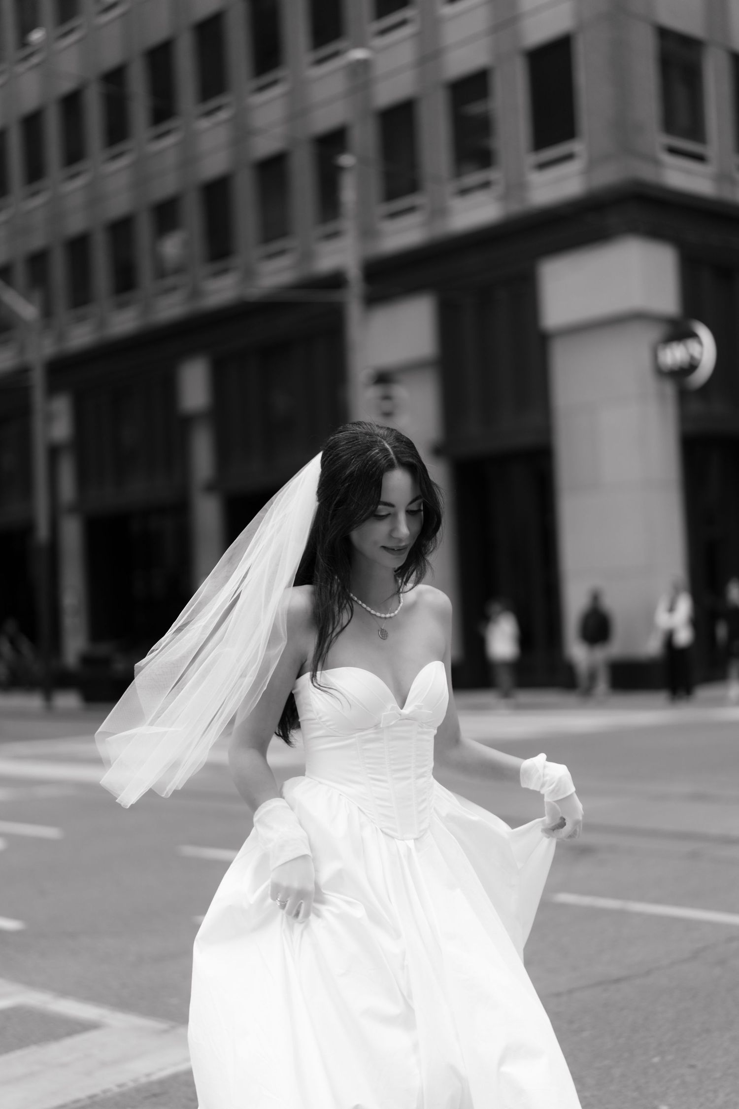 A bride in a flowing white wedding dress twirls gracefully on an empty urban street in black and white.