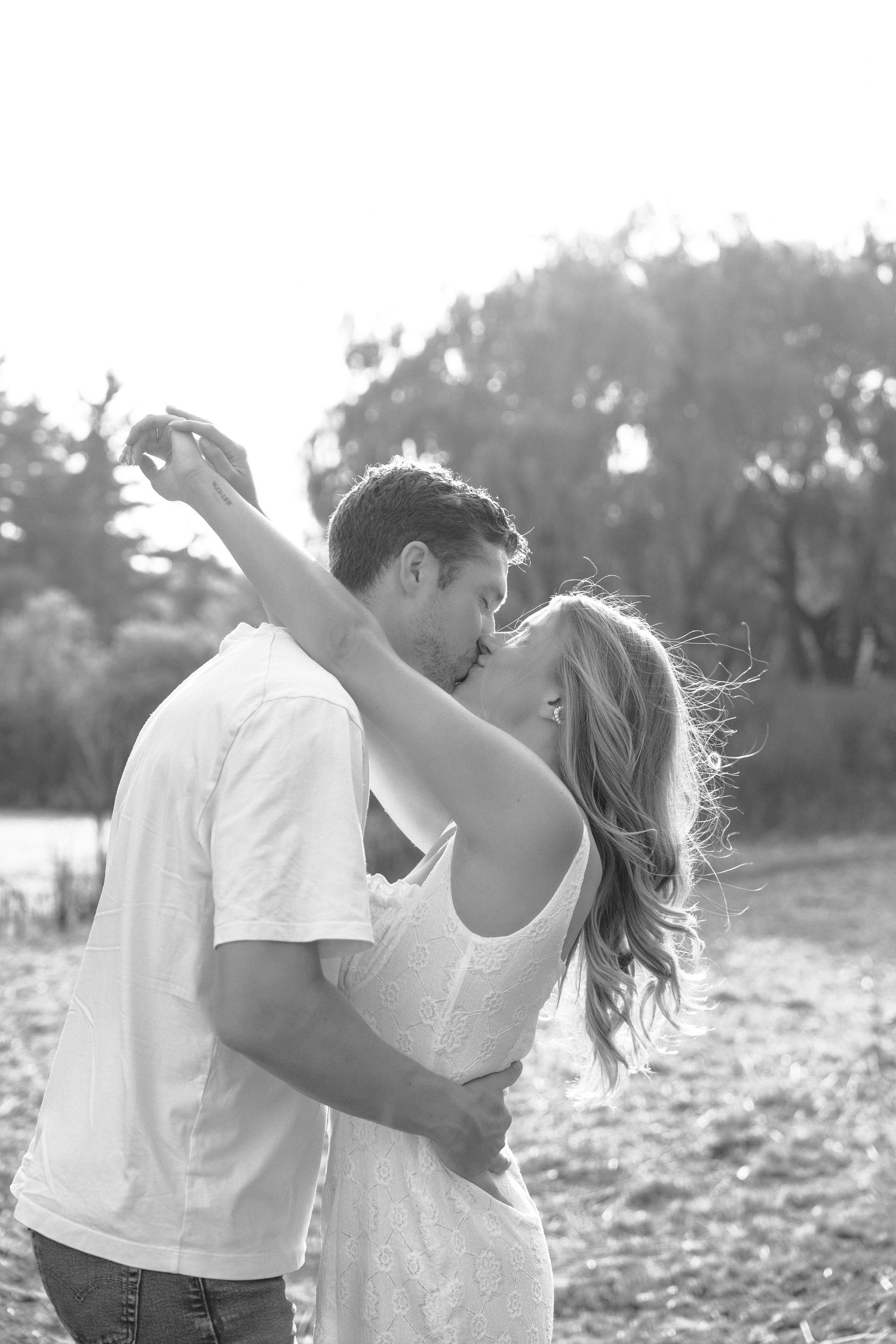 A romantic black and white photo series showing a couple embracing and dancing in a sunlit outdoor field.