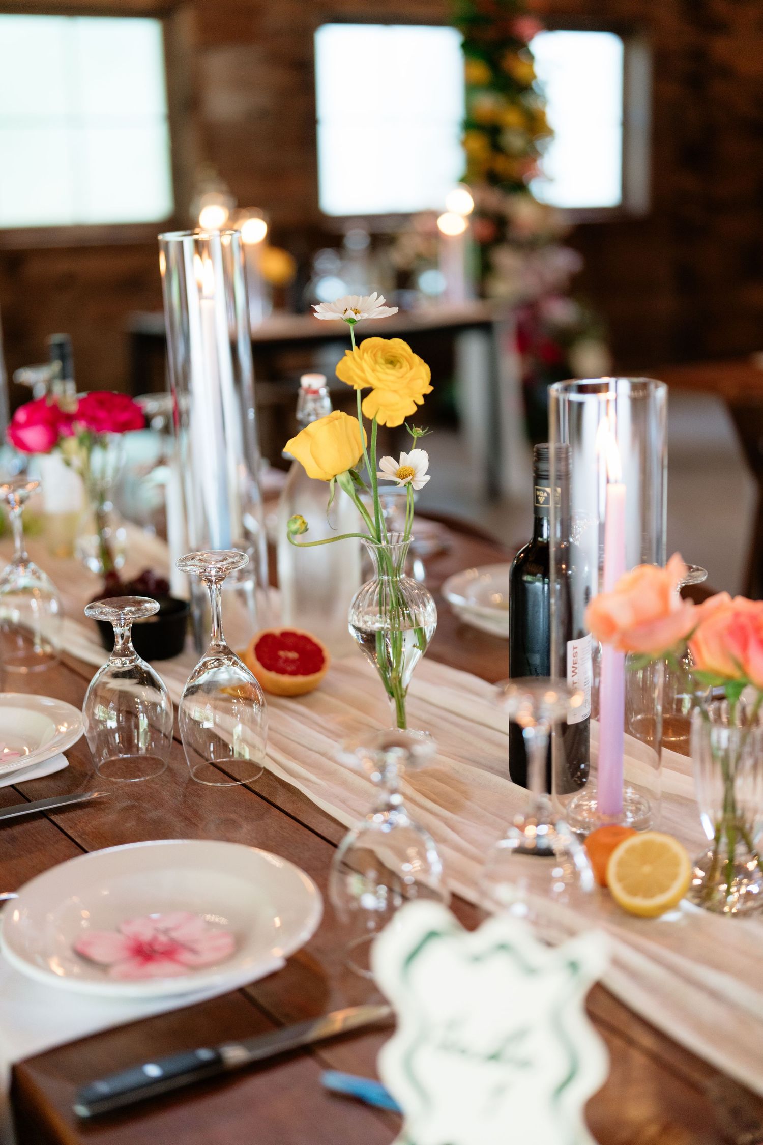 Elegant table settings at a wedding reception with delicate flowers in glass vases and citrus accents.