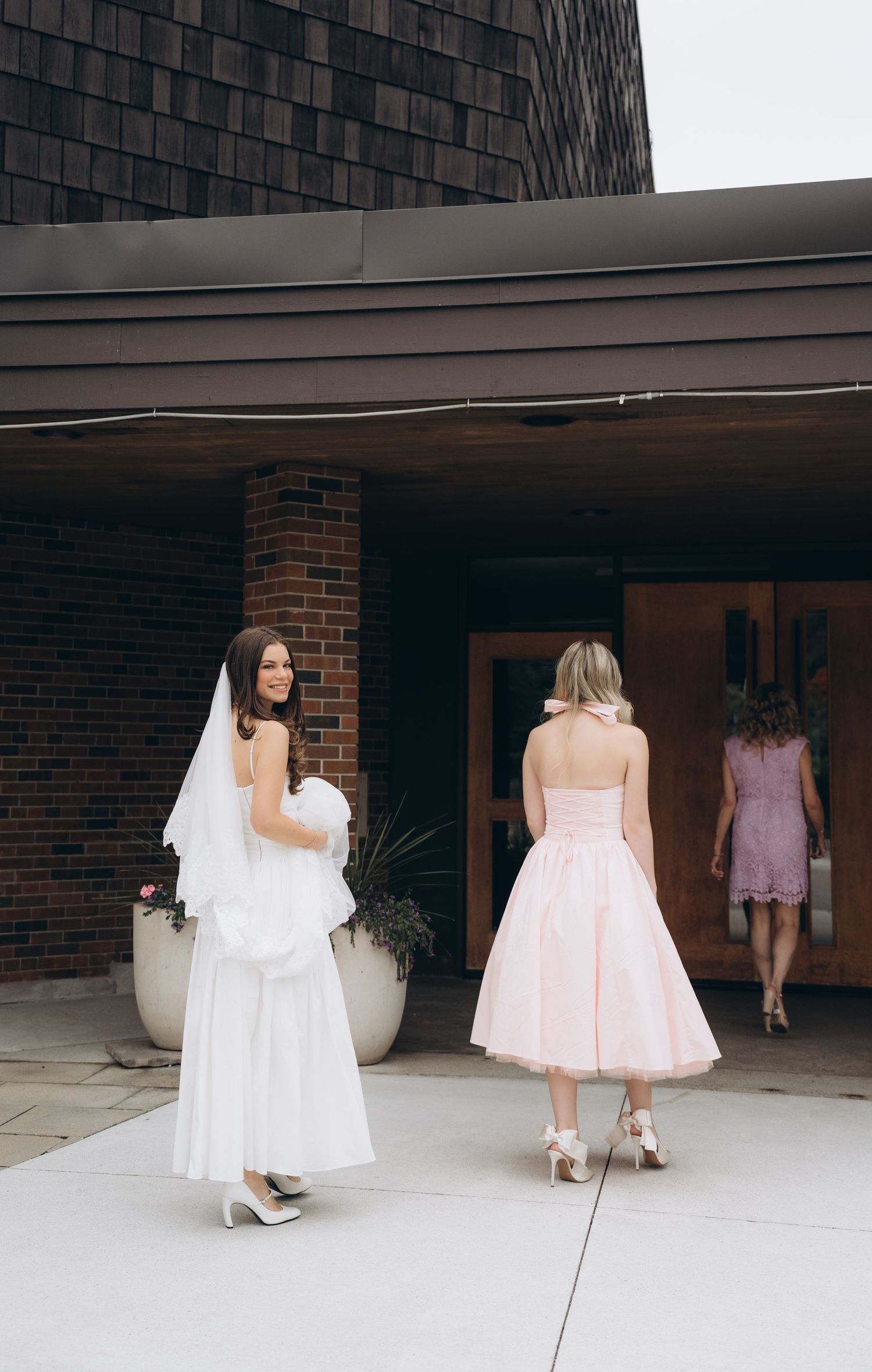 Multiple frames showing bridesmaids in pink dresses and a bride in white walking outside a brick building.
