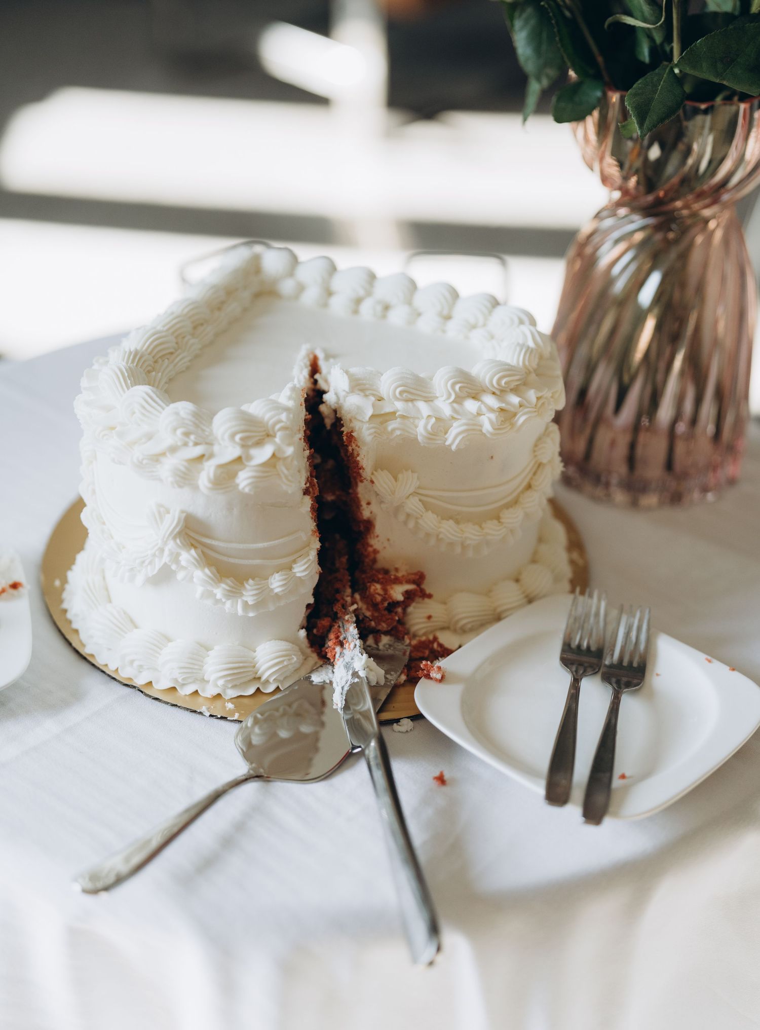 A white frosted layer cake being sliced to reveal chocolate cake layers and filling inside.