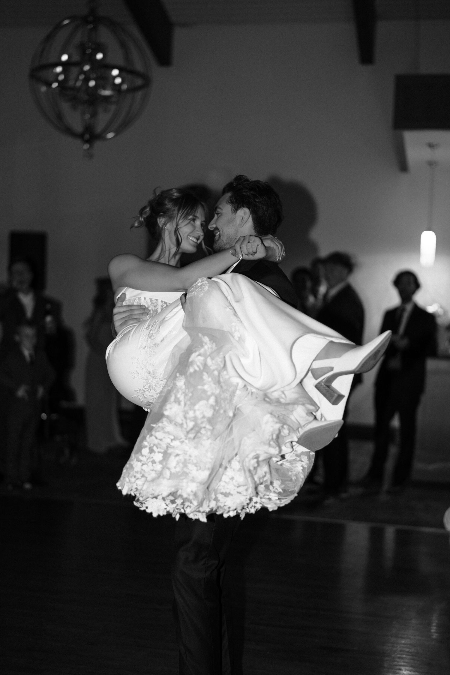 A close-up view of a white lace wedding dress twirling on a dark dance floor at a reception.