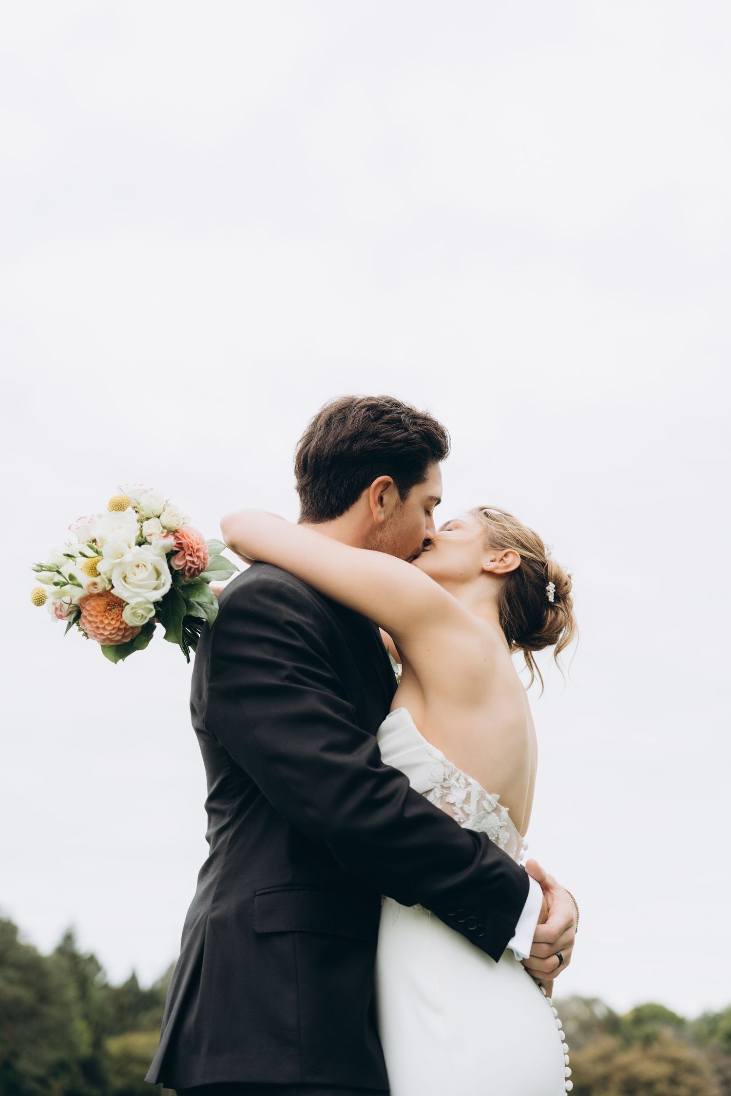 Romantic wedding couple dancing and embracing outdoors with white floral bouquet in a candid moment.