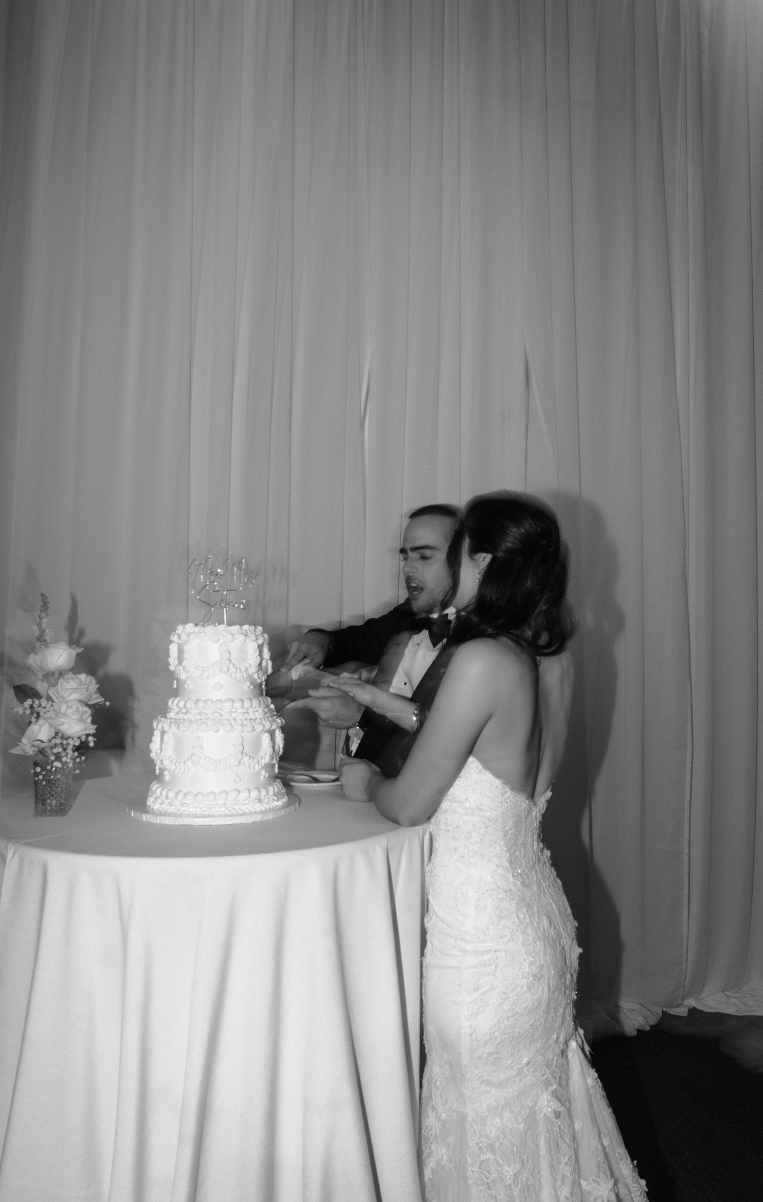 A black and white wedding photo series showing a couple kissing behind their wedding cake at the reception.