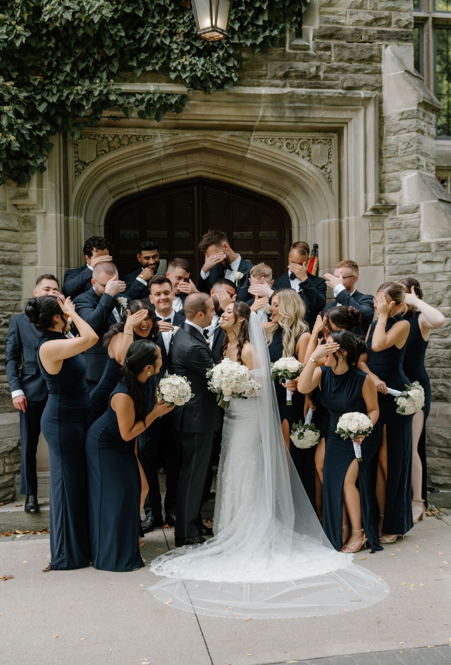 Wedding party in navy blue and white attire poses playfully in a sequence of shots outside a stone church building.