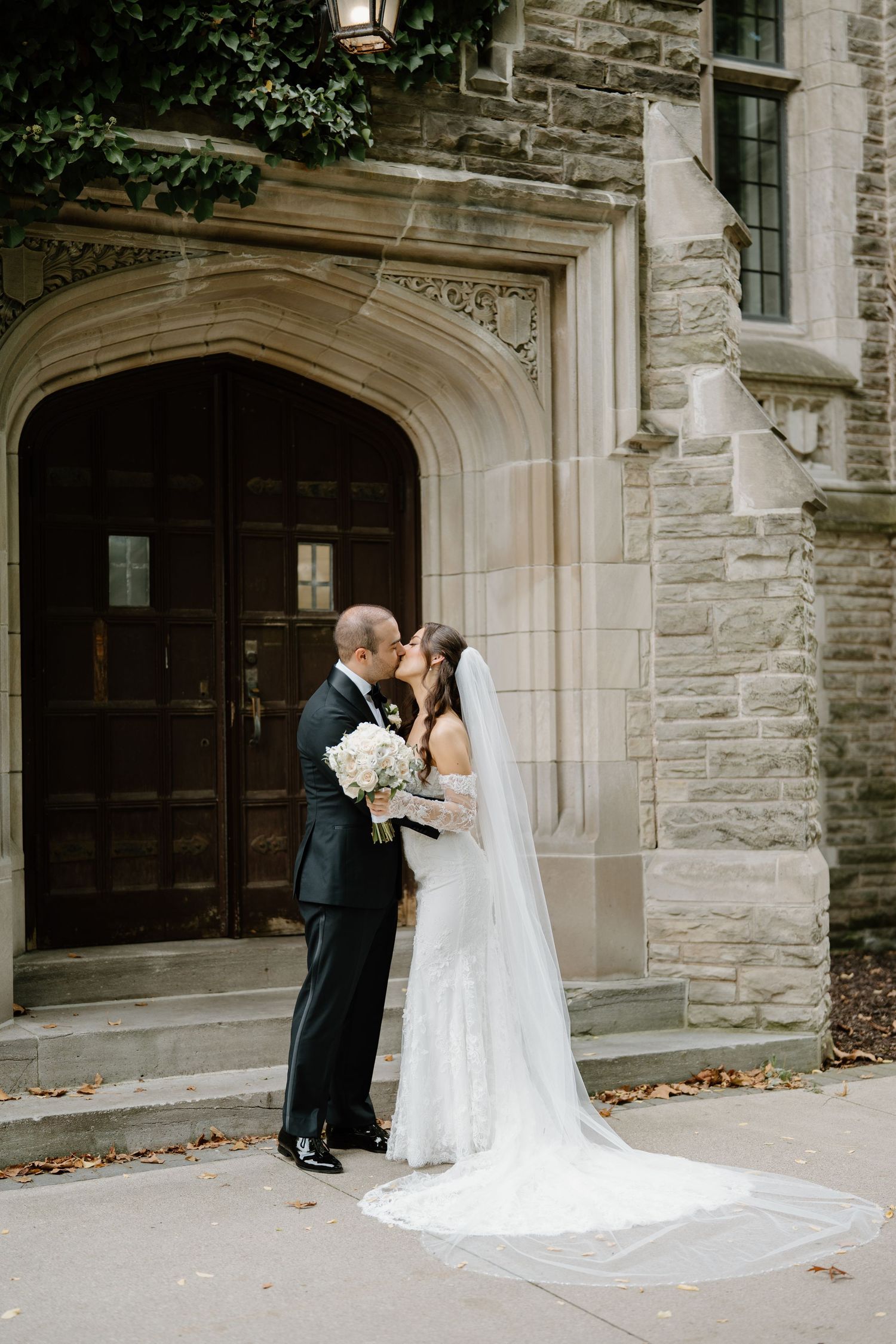 A wedding couple shares a tender kiss in front of an elegant stone church entrance.