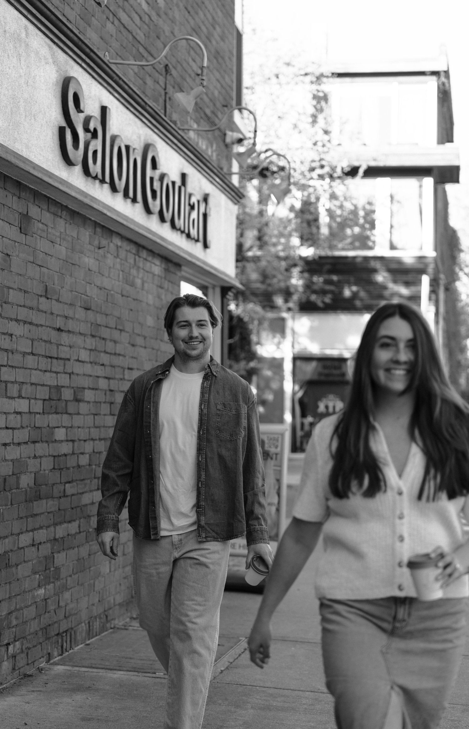 A black and white photograph shows two people walking past a storefront with a Salon Centric sign.
